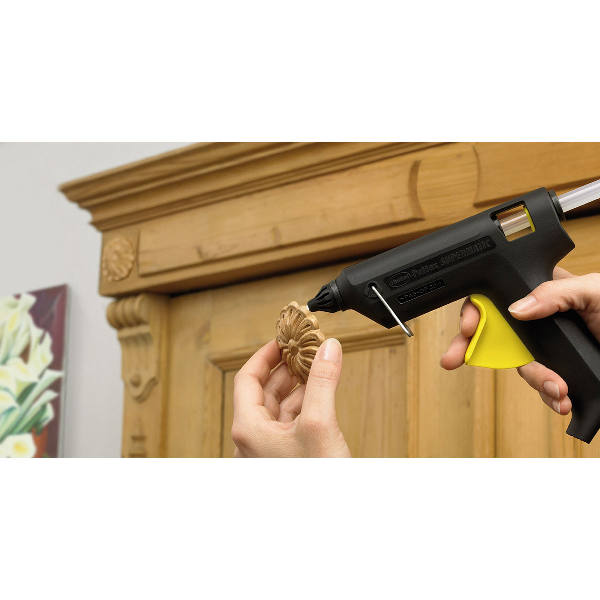 Hand verwendet eine Heißklebepistole auf einem Holzdekor vor einem Holzschrankhintergrund.