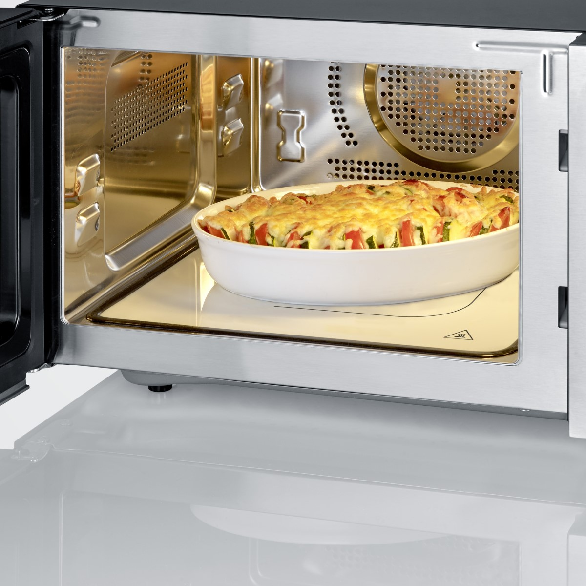 Otwarty piekarnik mikrofalowy z naczyniem żaroodpornym z pieczonym jedzeniem. Wnętrze ze stali nierdzewnej.