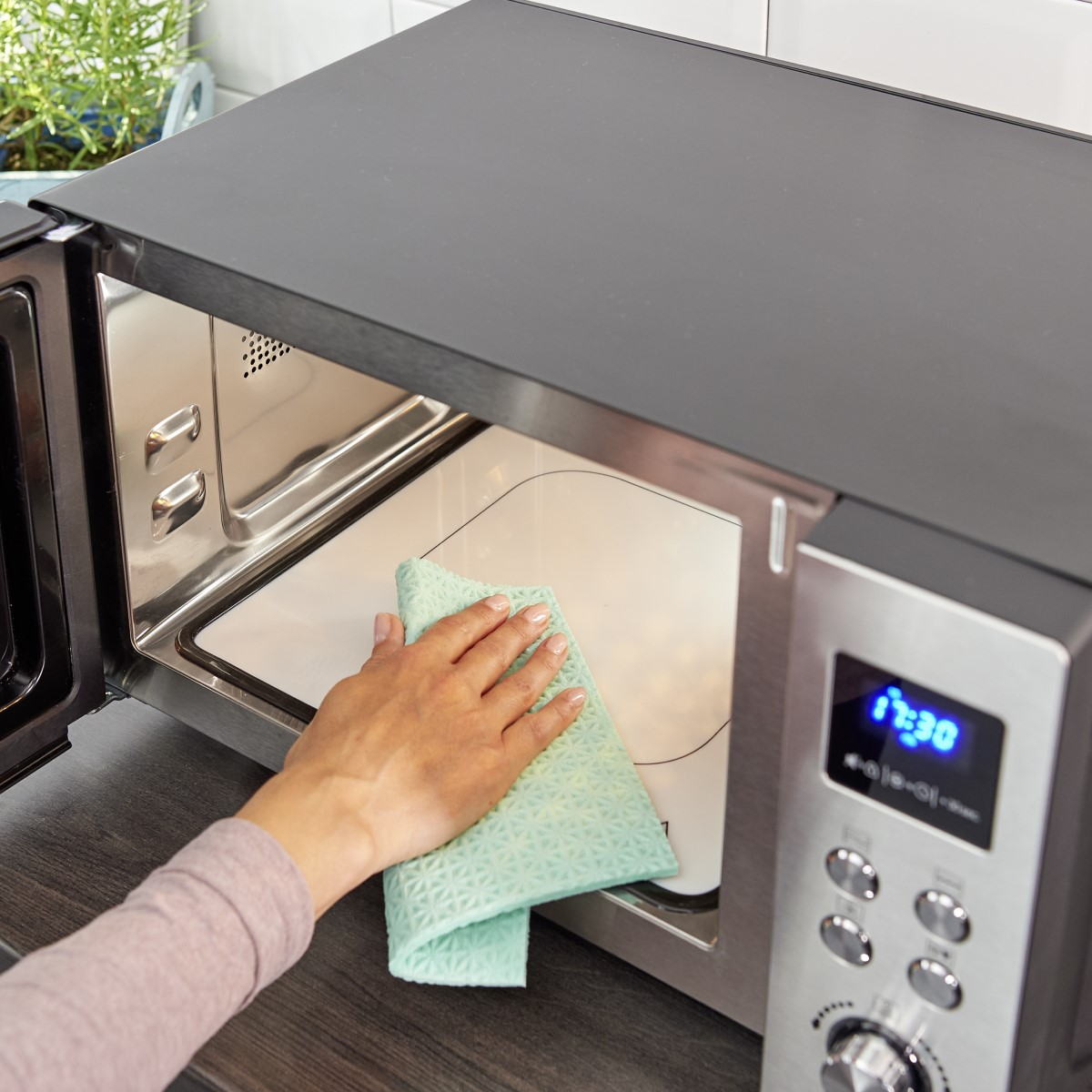 Osoba wyciera wnętrze kuchenki mikrofalowej szmatką.