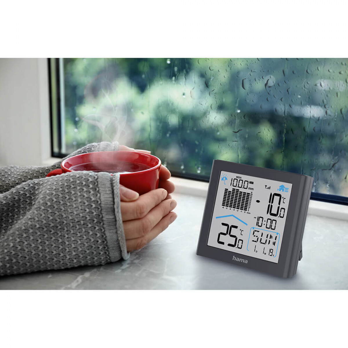 Dłonie trzymające czerwony kubek, w pobliżu okna ze stacją pogodową.