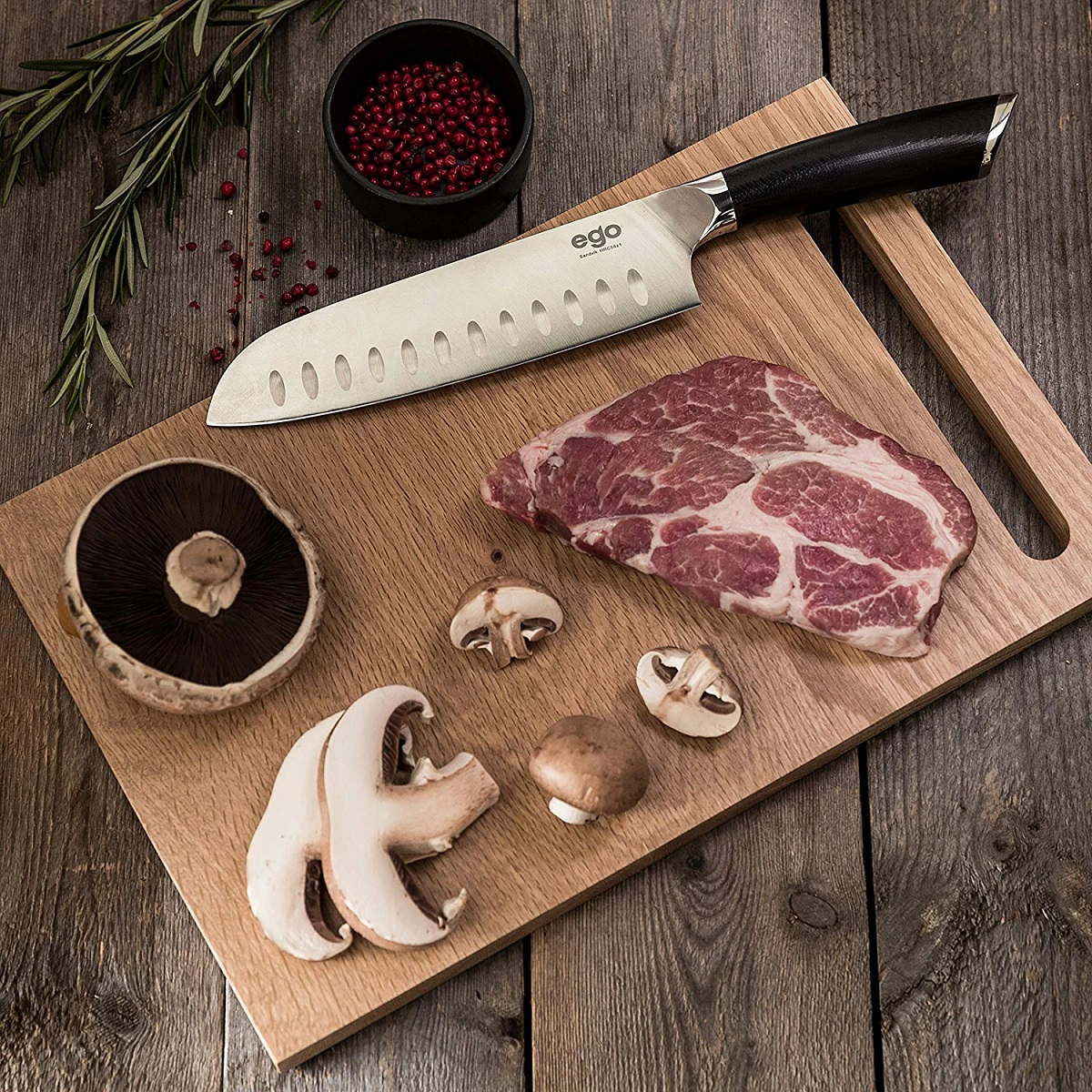 Messer auf Holzbrett mit Steak, Pilzen und einer Schüssel Pfefferkörnern.