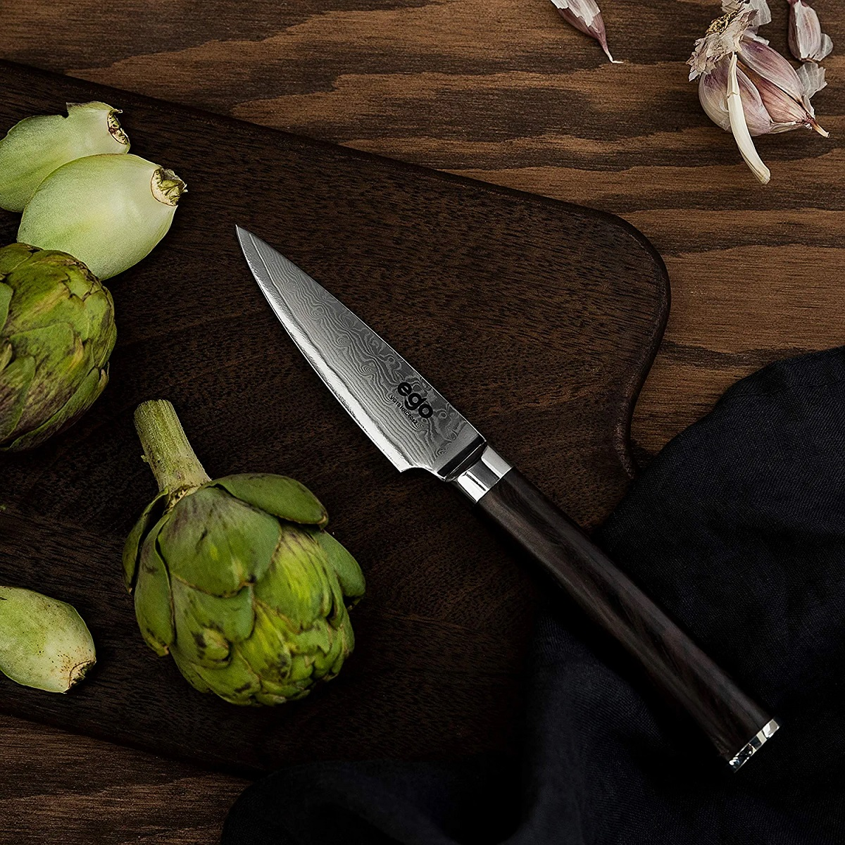 Messer auf Schneidebrett mit Artischocken und Knoblauch. Holzuntergrund.