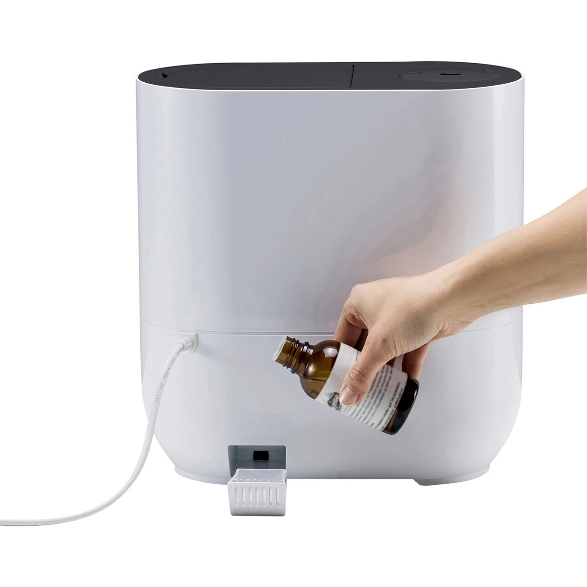 Weißer Luftbefeuchter, in den eine Hand Flüssigkeit aus einer braunen Flasche gießt.