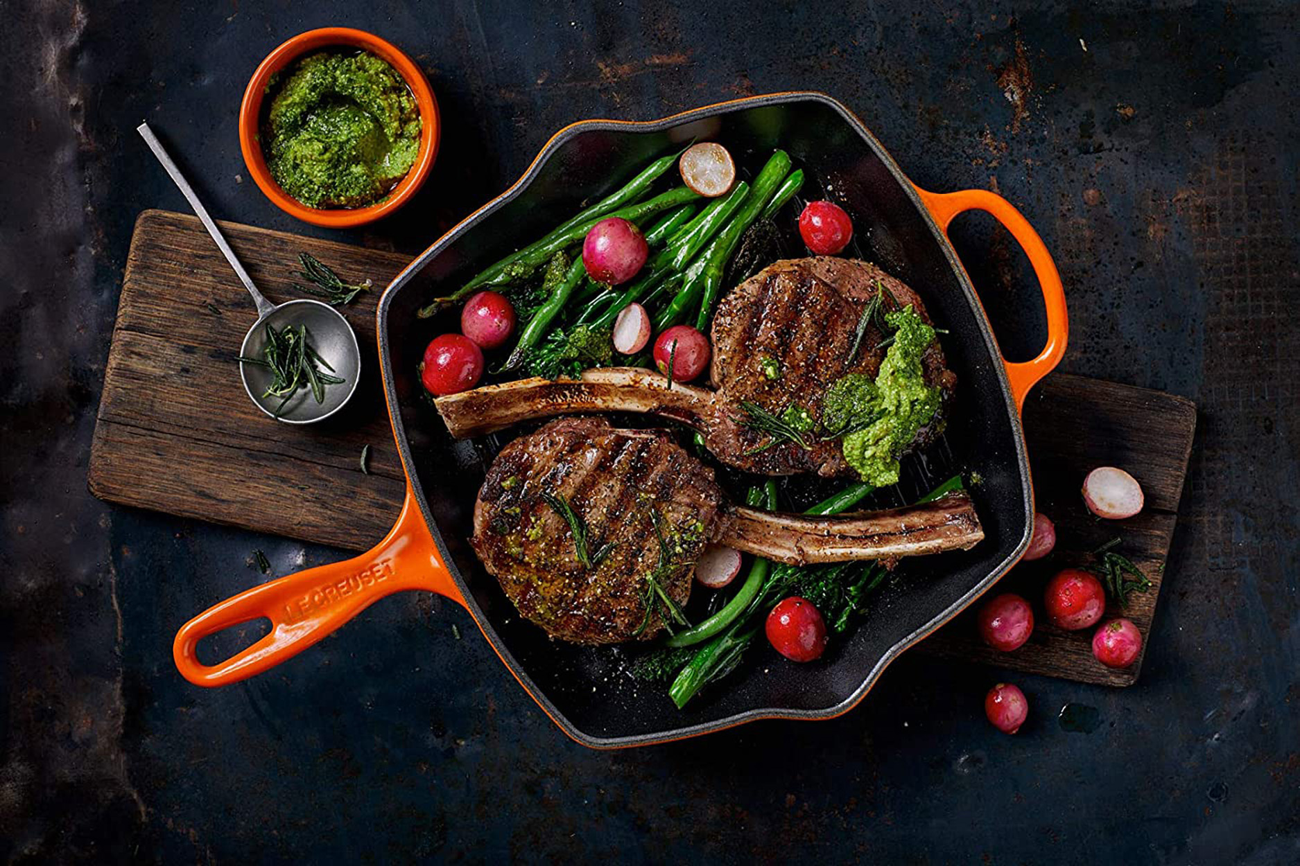 Zwei gegrillte Ribeye-Steaks in einer orangefarbenen Le Creuset-Pfanne mit grünen Bohnen und Radieschen.