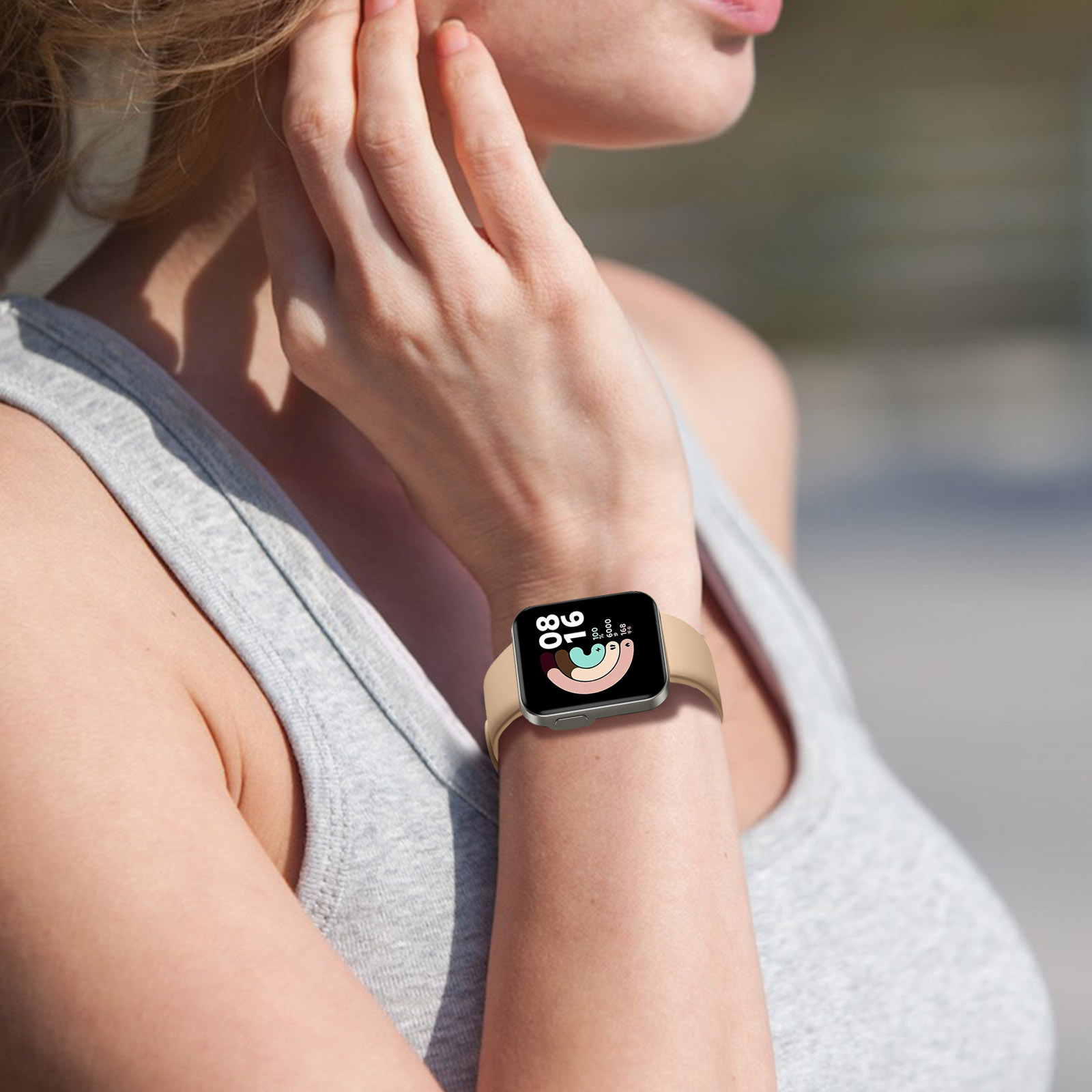 Smartwatch en muñeca, camiseta sin mangas gris, vegetación detrás.
