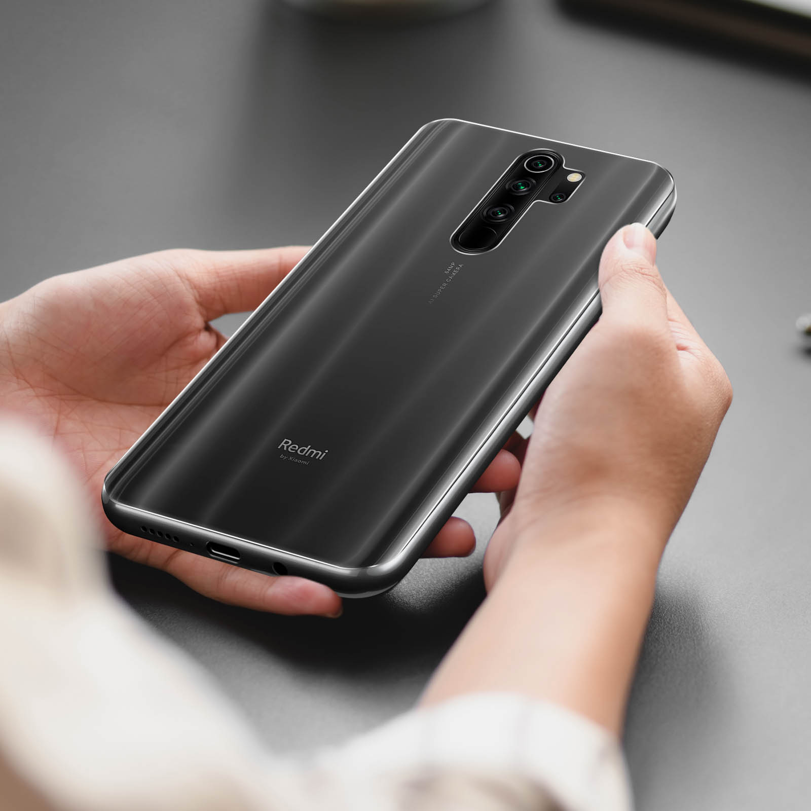 Mani che tengono un telefono Redmi nero. Il telefono ha più fotocamere e un design elegante. Lo sfondo è una superficie grigia.