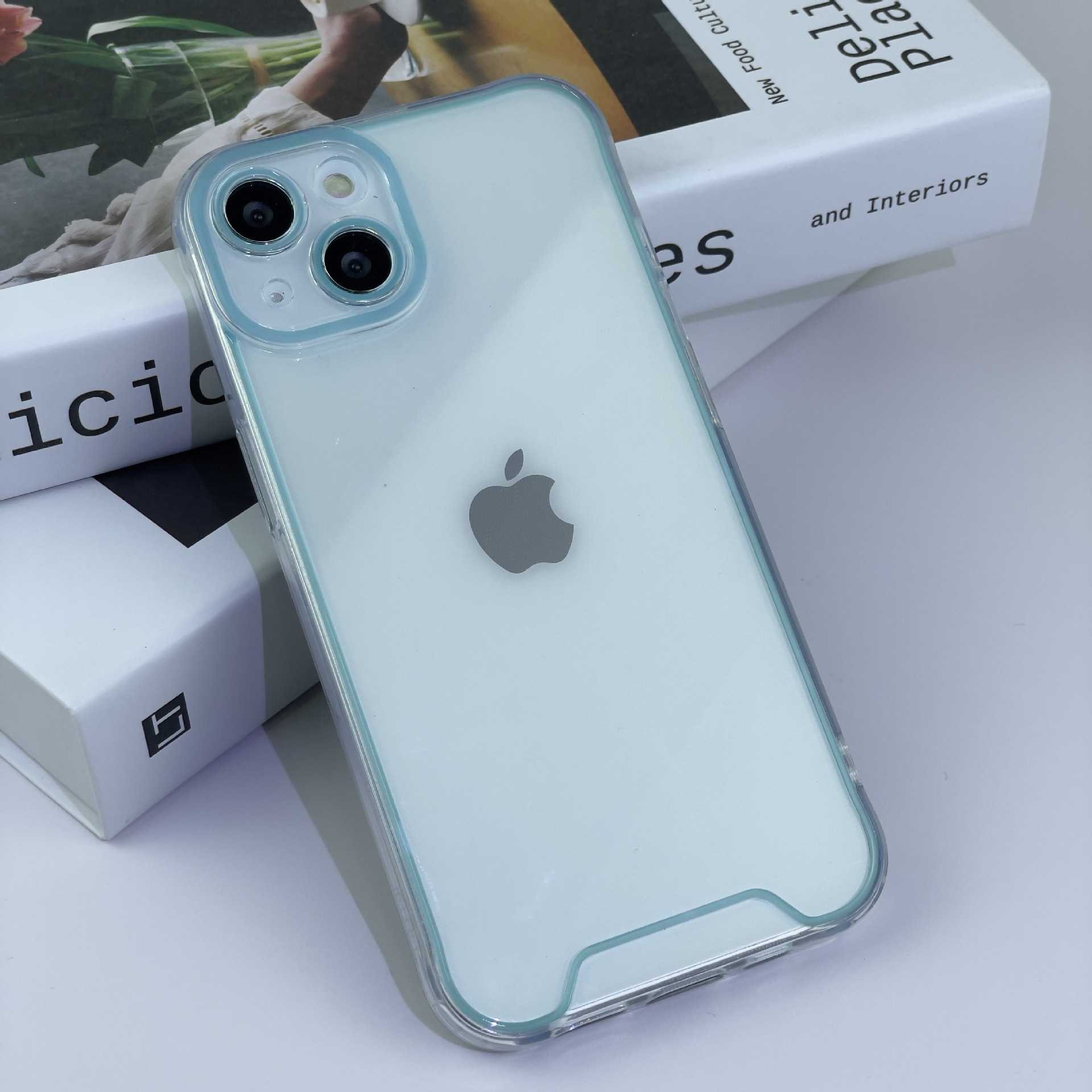Ein Mobiltelefon mit transparentem Gehäuse auf zwei Büchern. Das Telefon hat eine türkisfarbene Umrandung.