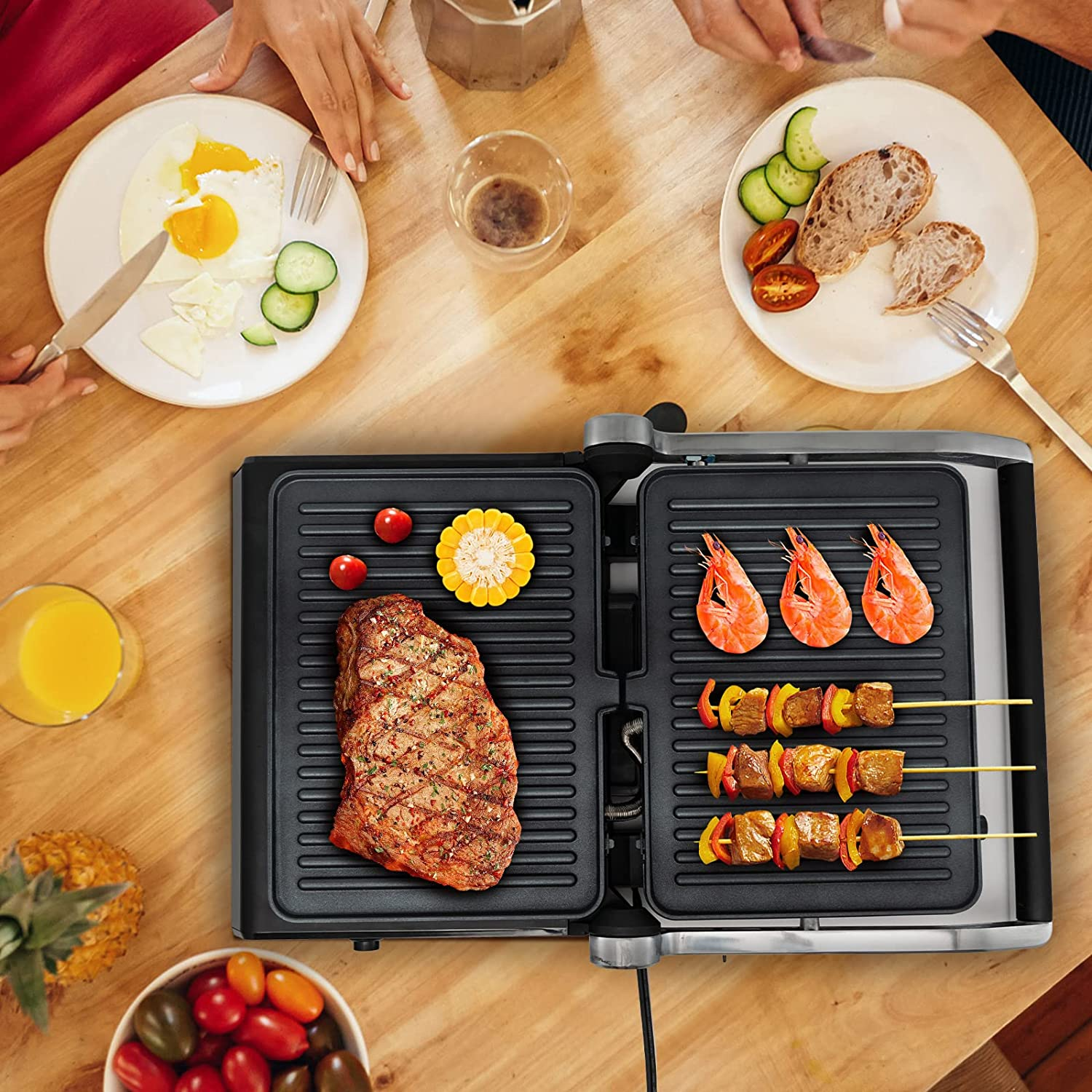Ein Grill mit Essen, darunter Steak, Garnelen und Gemüse. Es gibt Teller mit Essen und Getränken.