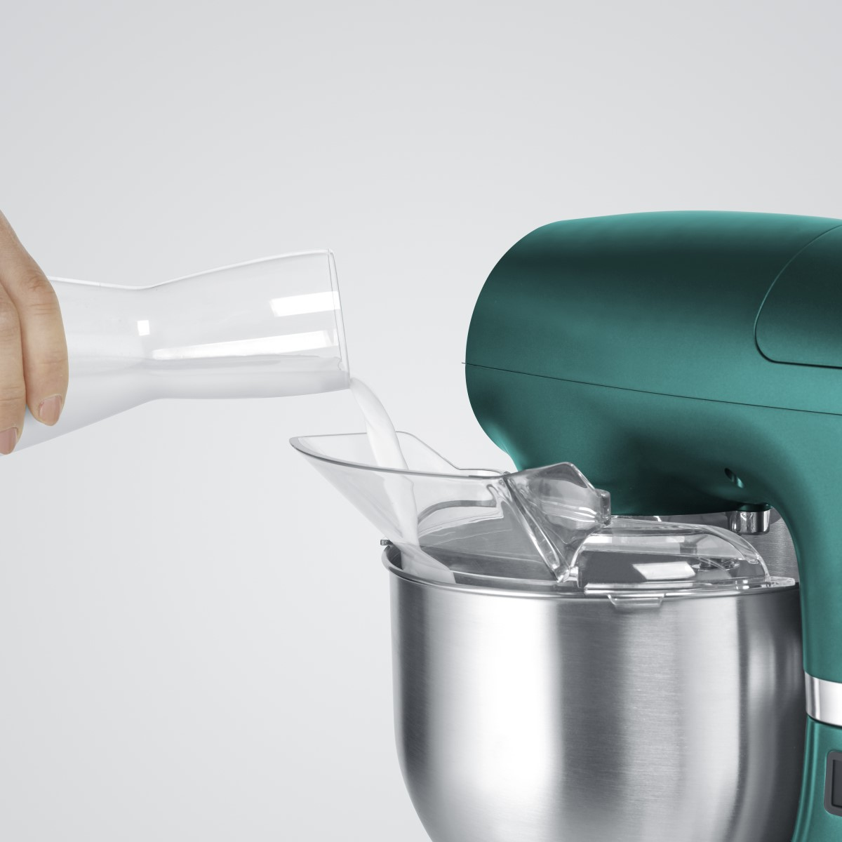 Eine Hand gießt Milch in einen türkisfarbenen Standmixer. Der Mixer hat einen transparenten Spritzschutz.