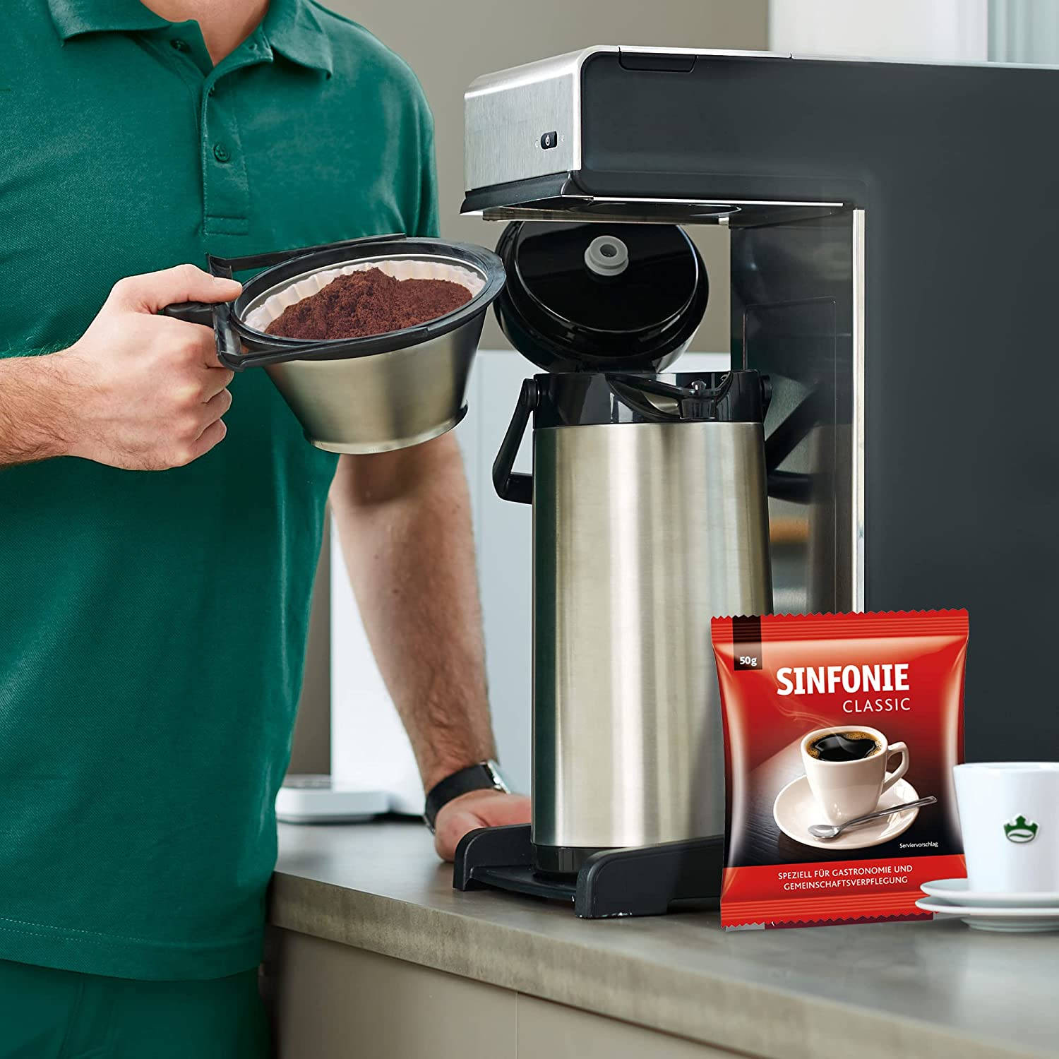 Una persona tiene in mano un filtro con fondi di caffè sopra una macchina da caffè, con un sacchetto di caffè accanto.