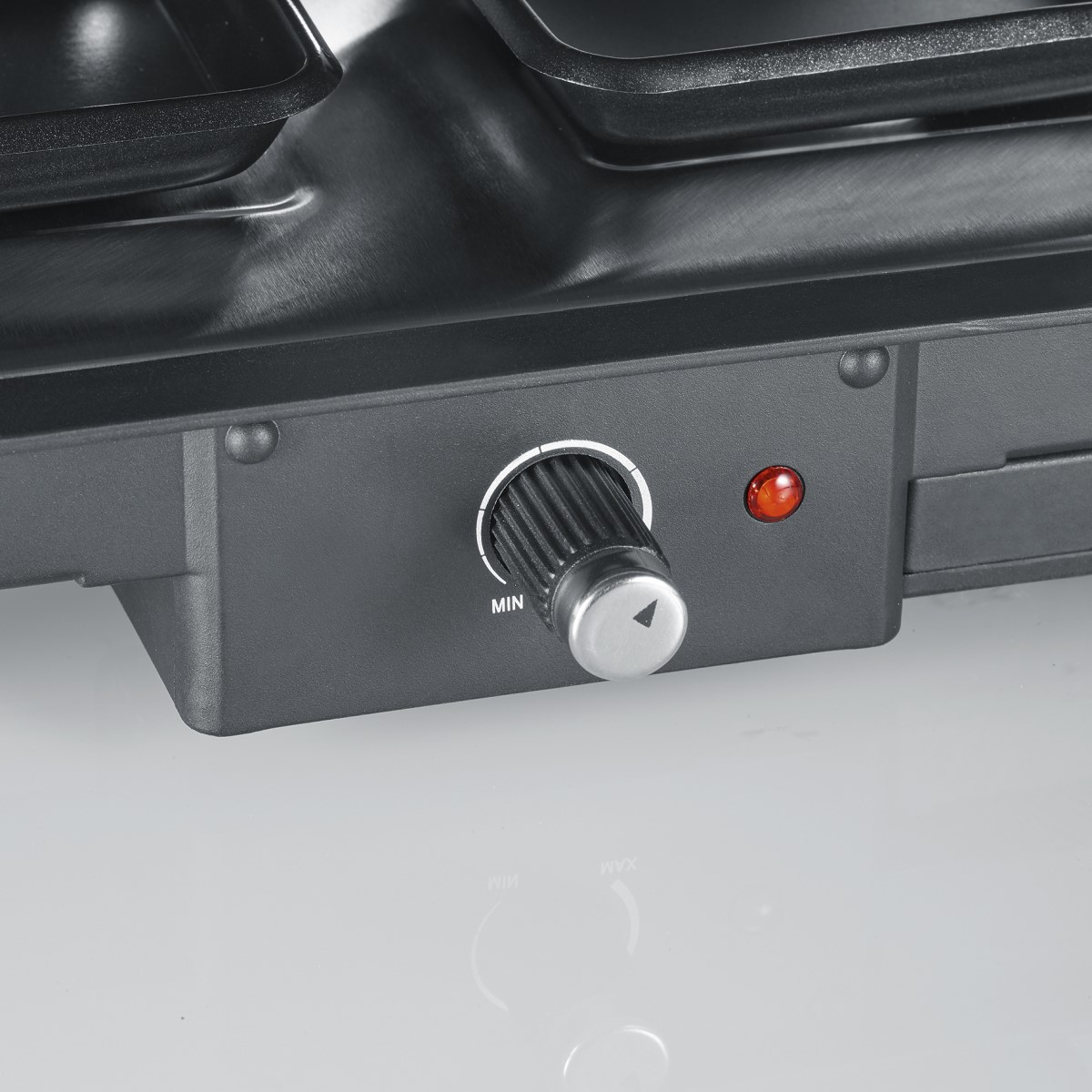 Close-up of a black raclette grill control panel with a dial and a red power light.