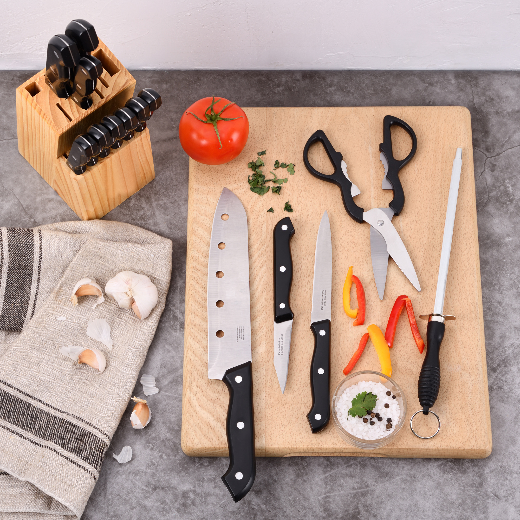Una escena de cocina con una tabla de cortar de madera, cuchillos, tomates, ajo, tijeras y otras herramientas de cocina.