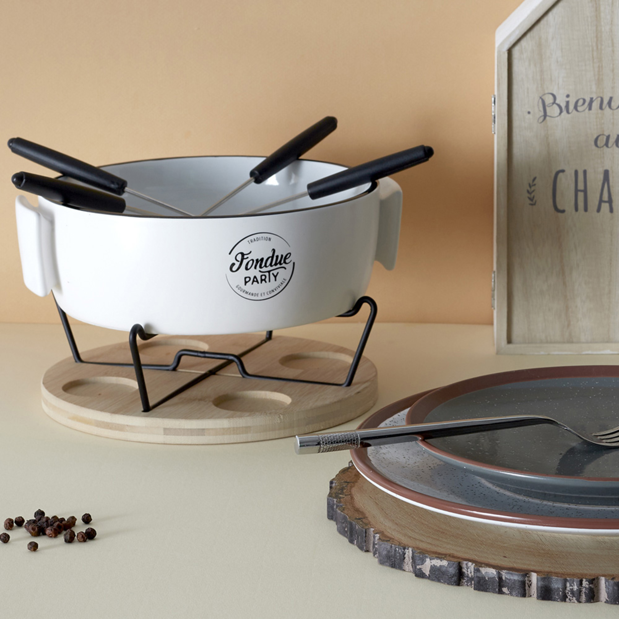 Set per fondue con pentola bianca, piatti, supporto in legno e cartello in legno.