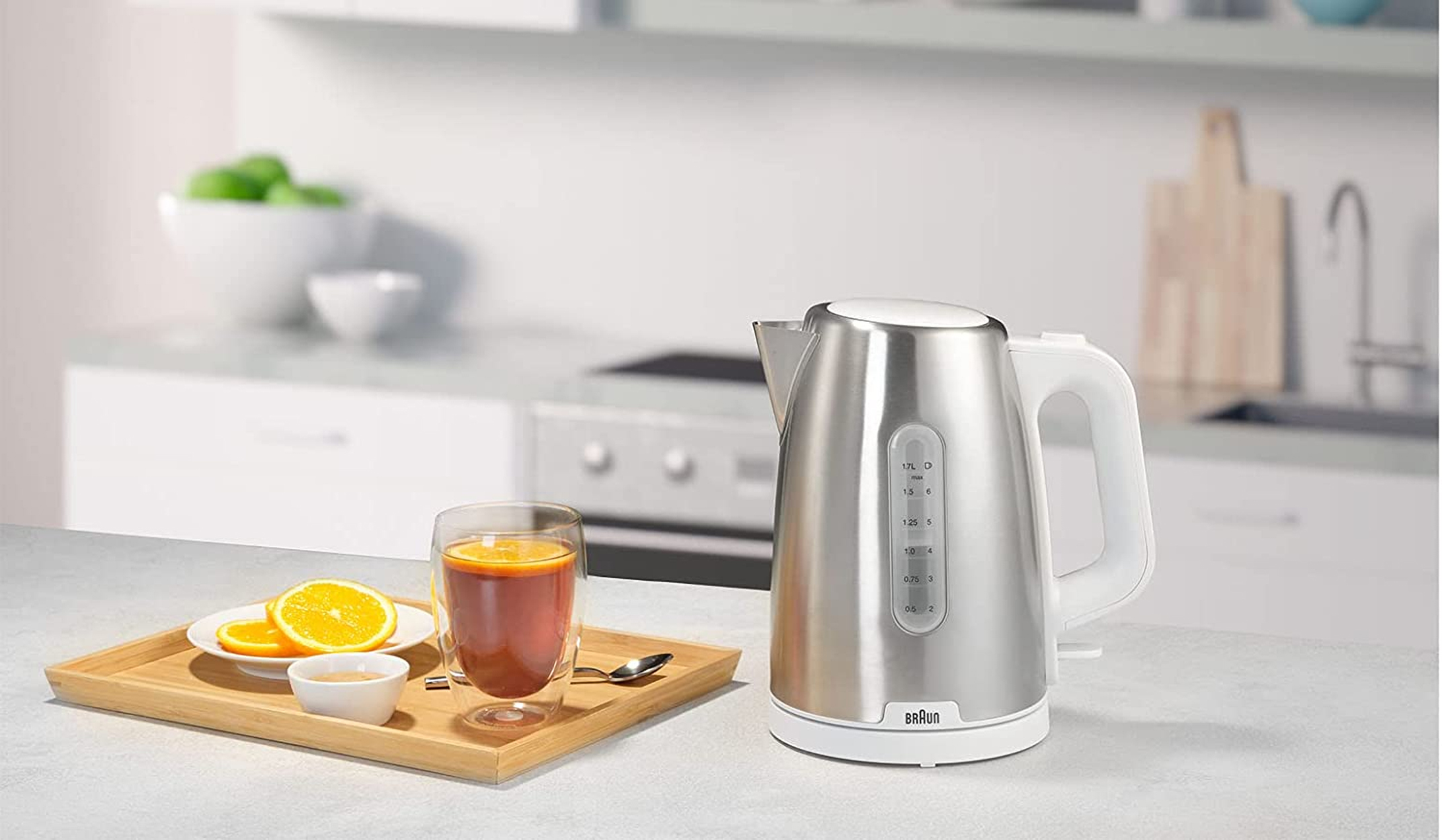 Bouilloire électrique en acier inoxydable avec un verre, un plateau avec des oranges et une cuillère.