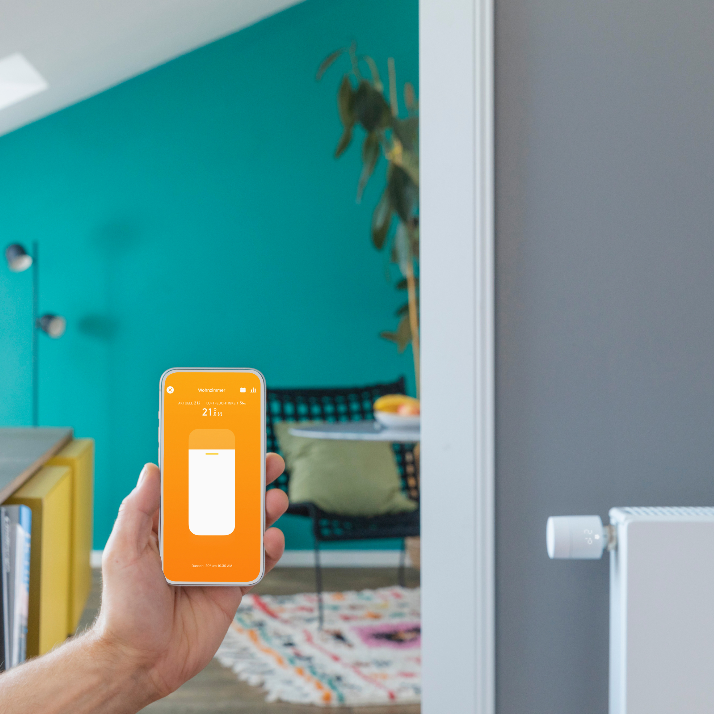 Eine Hand hält ein Telefon mit orangefarbenem Bildschirm vor einem Raum.