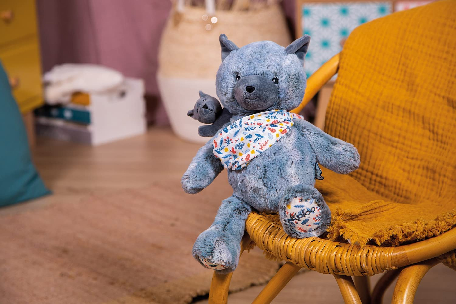 Un loup en peluche avec un petit jouet loup sur son épaule est assis sur une chaise en osier.