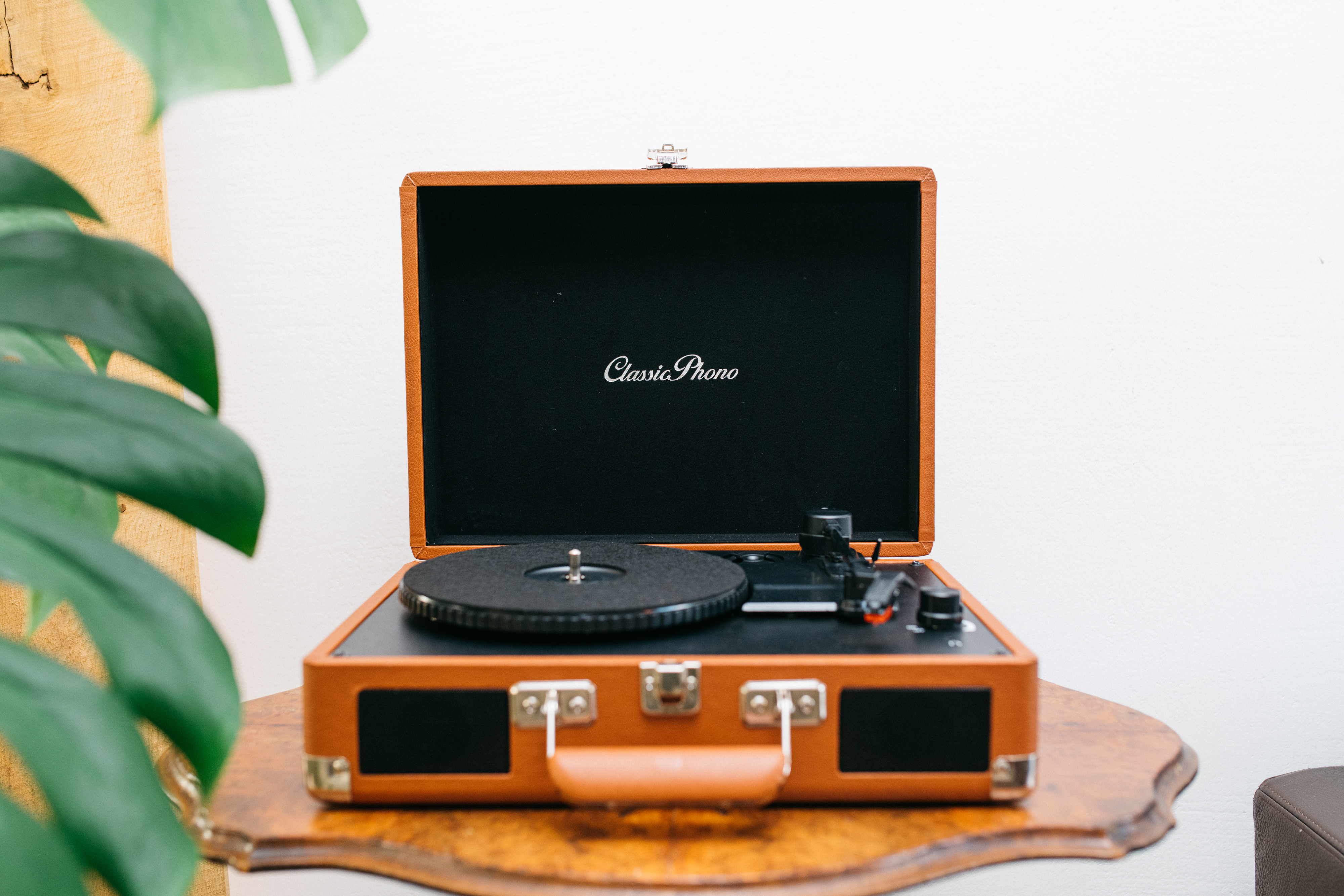 Brązowa, otwarta walizka z gramofonem w środku, na tle białej ściany.