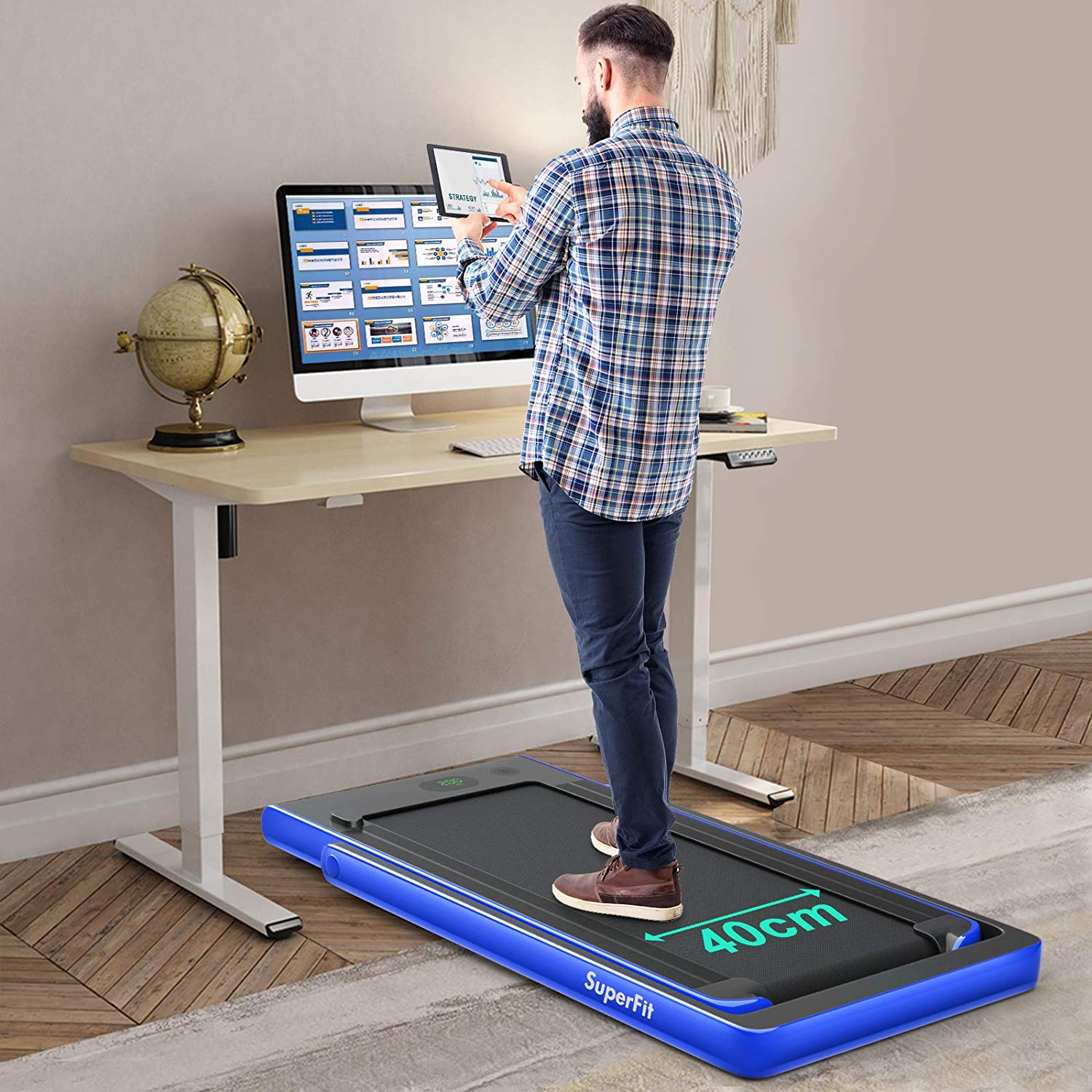Mann steht auf blauem Mini-Laufband am Schreibtisch. Computer und Globus auf dem Schreibtisch, Holzfußboden.