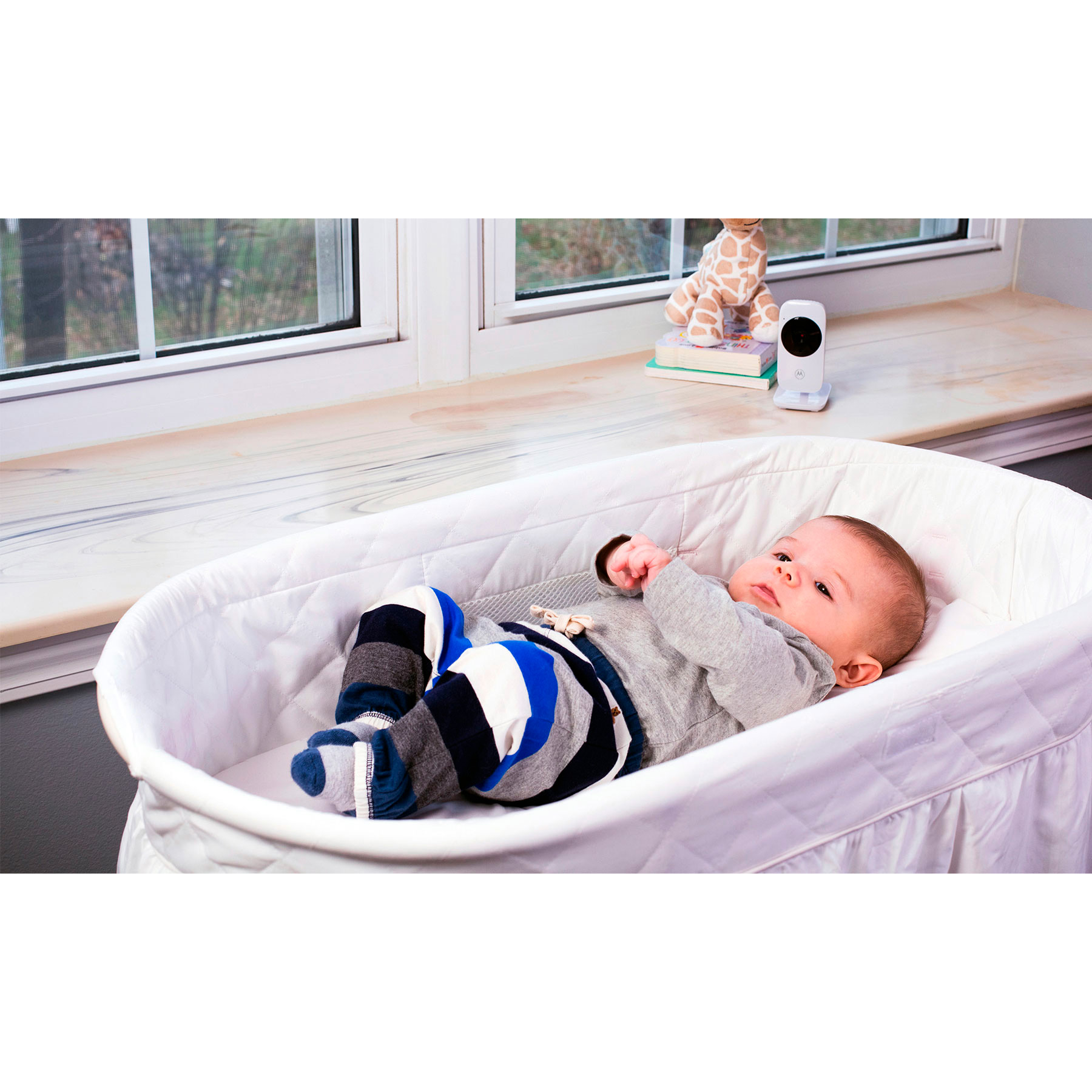 Baby in einer Babywiege. Babyphone und Giraffenspielzeug. Weißer Hintergrund.