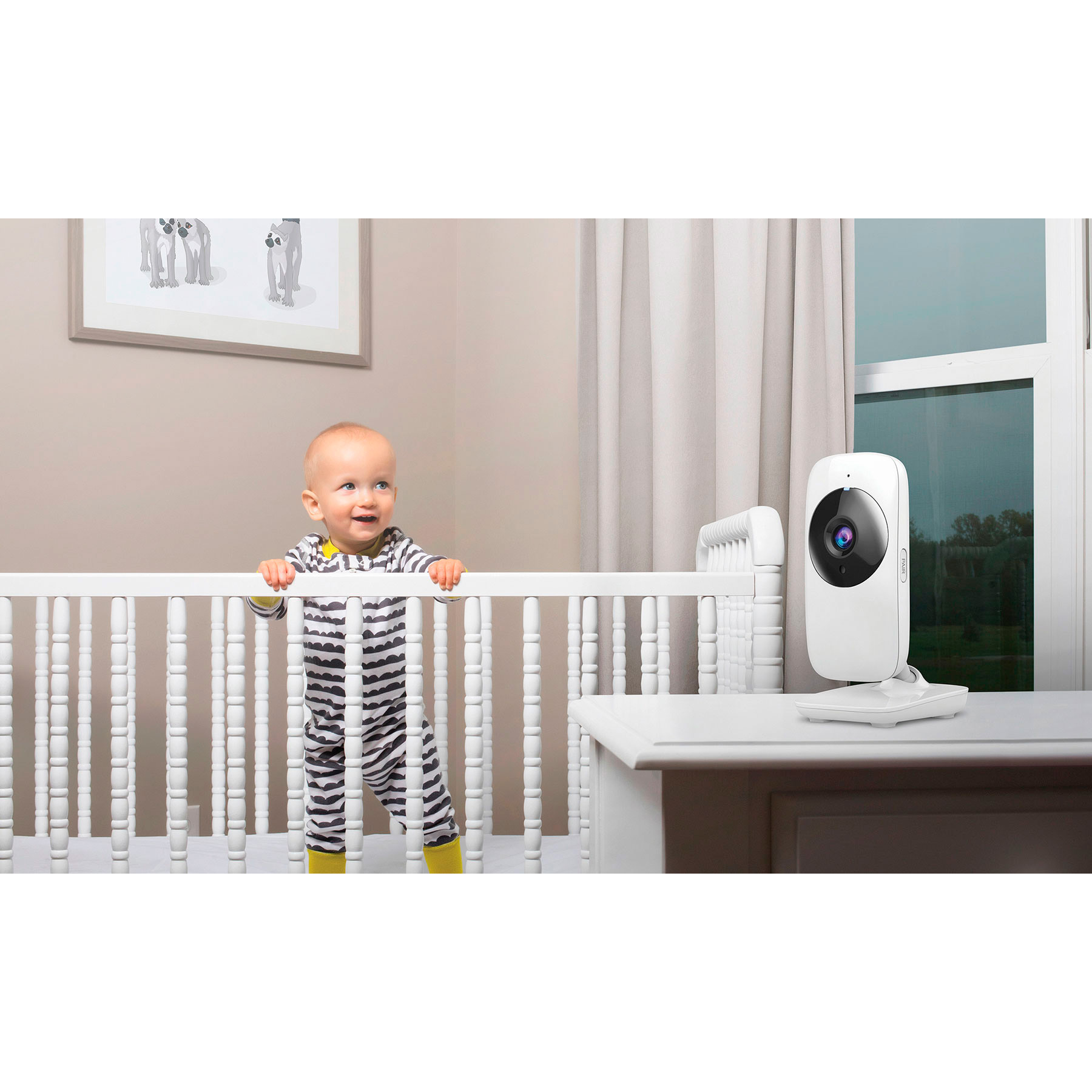 Baby in einem Kinderbett, das einen weißen Babyphone auf einem Tisch anschaut.
