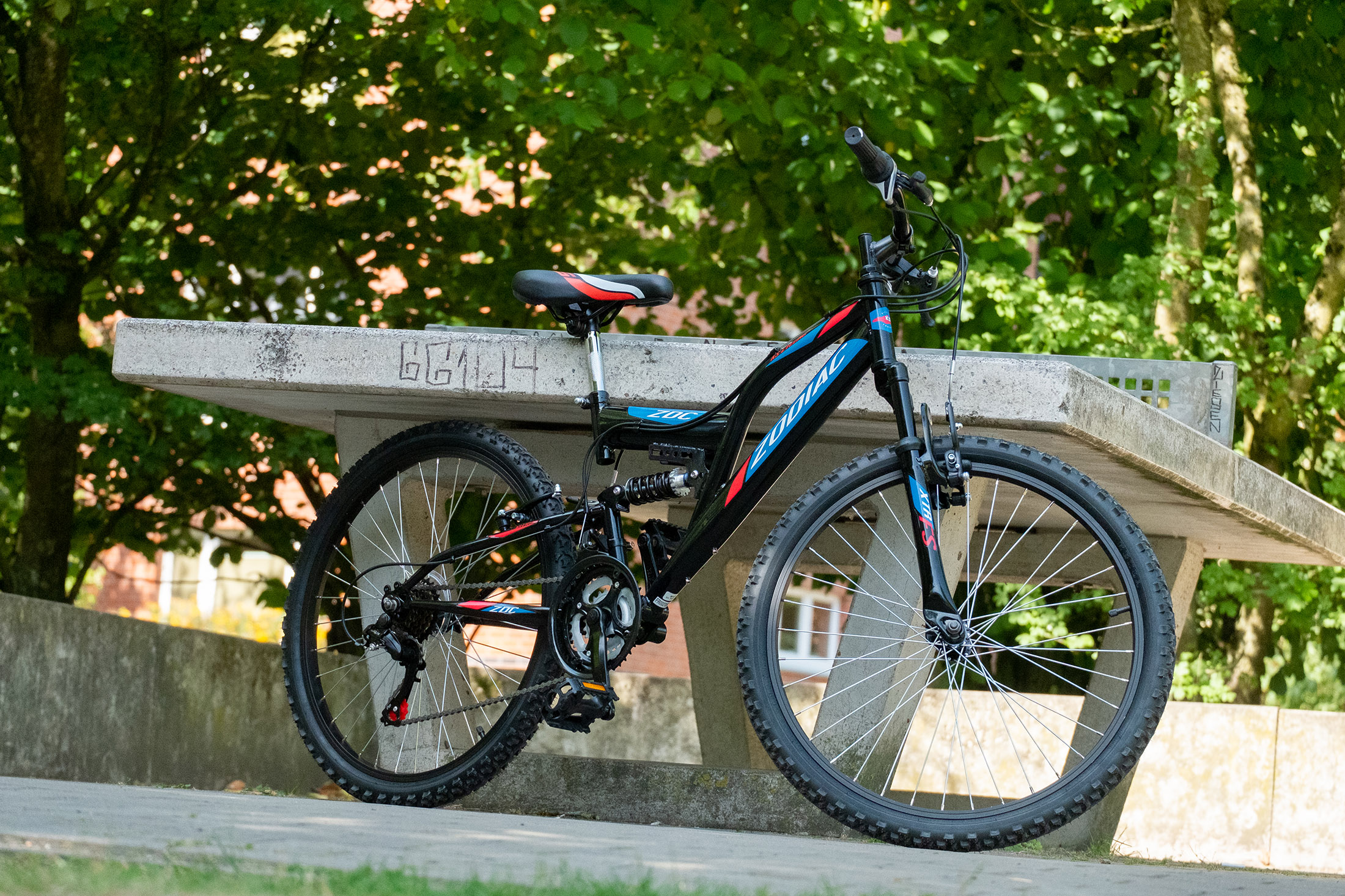 Mountainbike mit schwarzem Rahmen, blauen Akzenten und einem Parktisch im Hintergrund.
