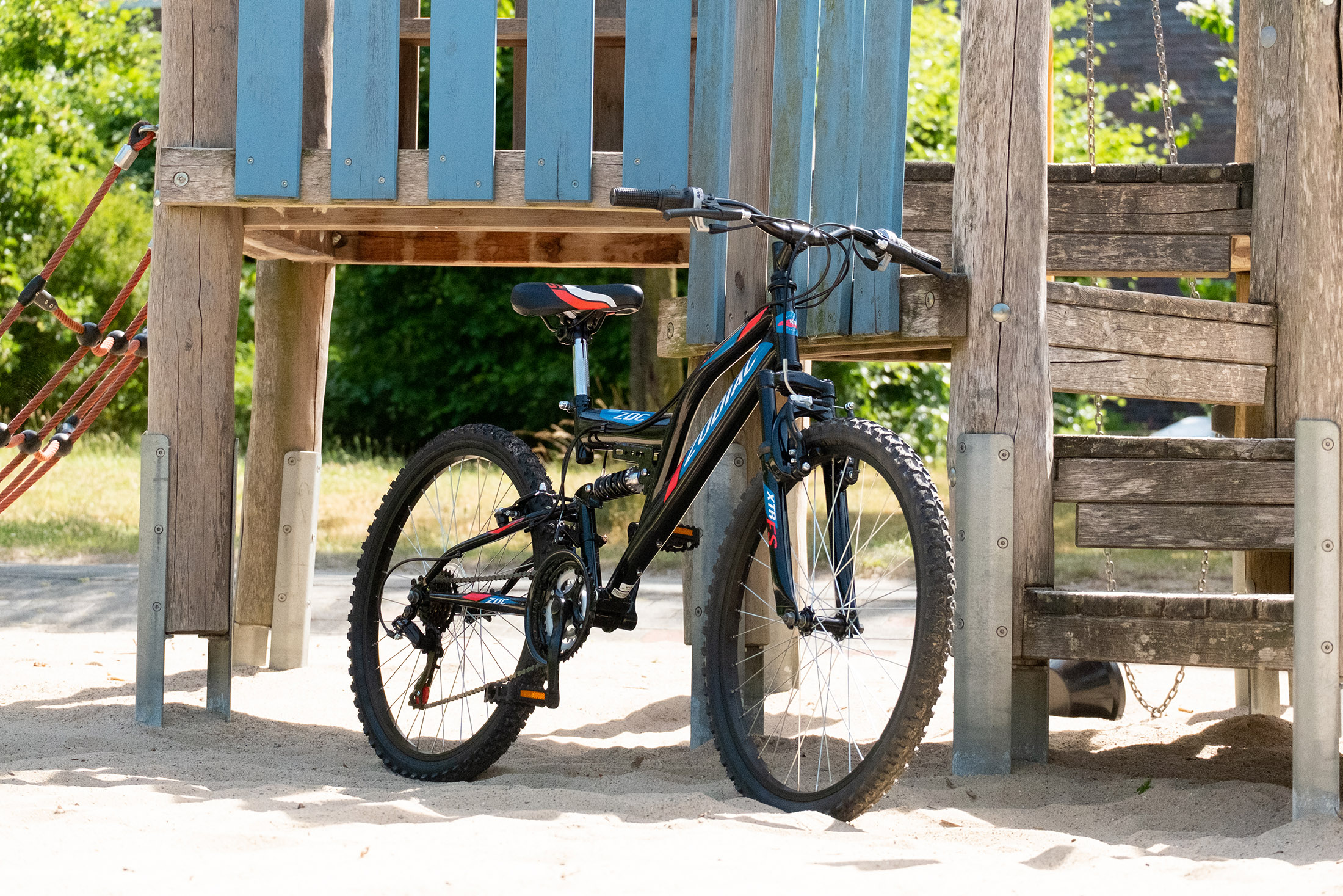 Schwarz-blaues Fahrrad. Es steht vor einem hölzernen Spielplatz.