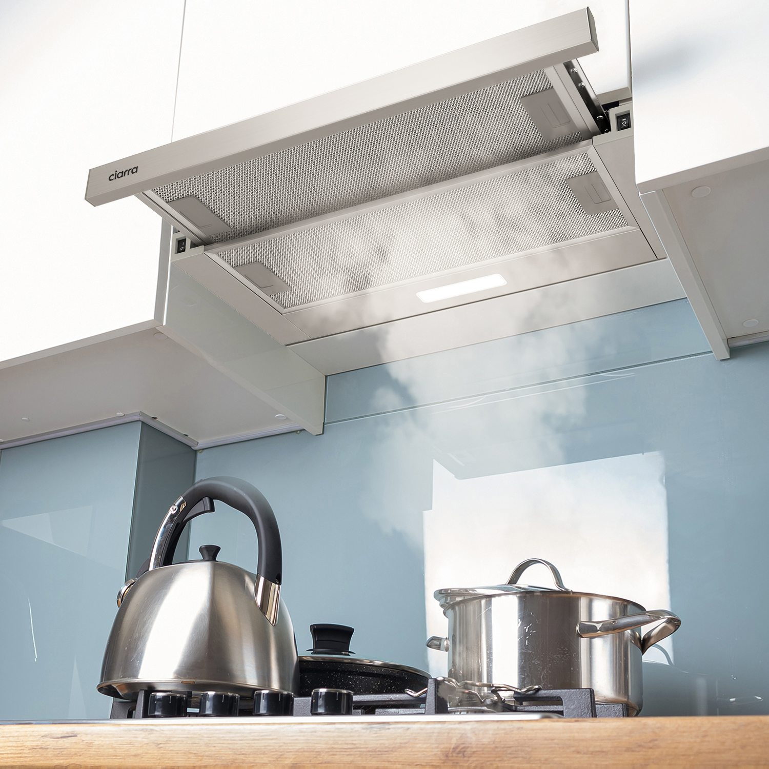 Kitchen hood above a stove with a kettle and pan. Blue wall background.
