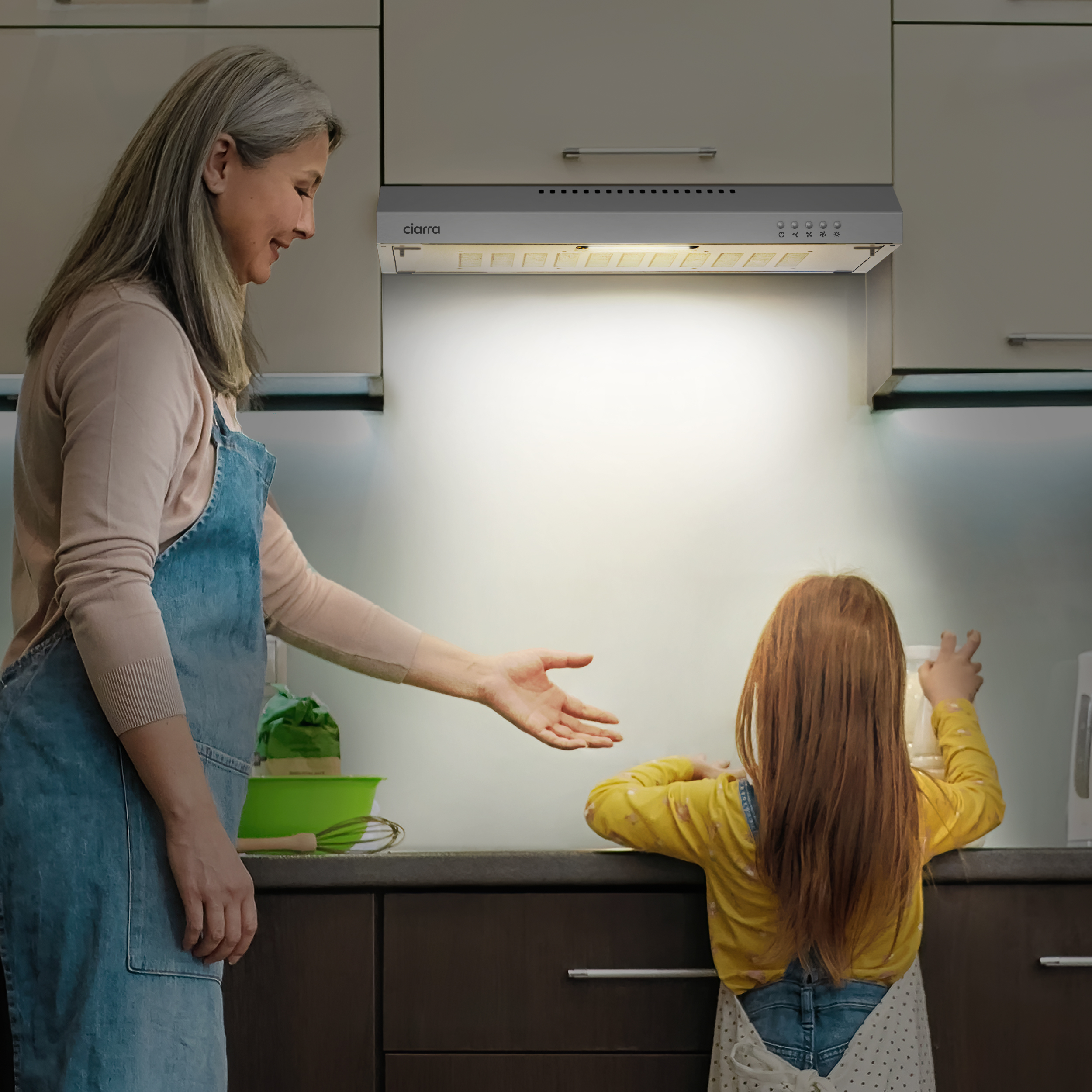 Een vrouw en een kind in de keuken kijken naar een afzuigkap.