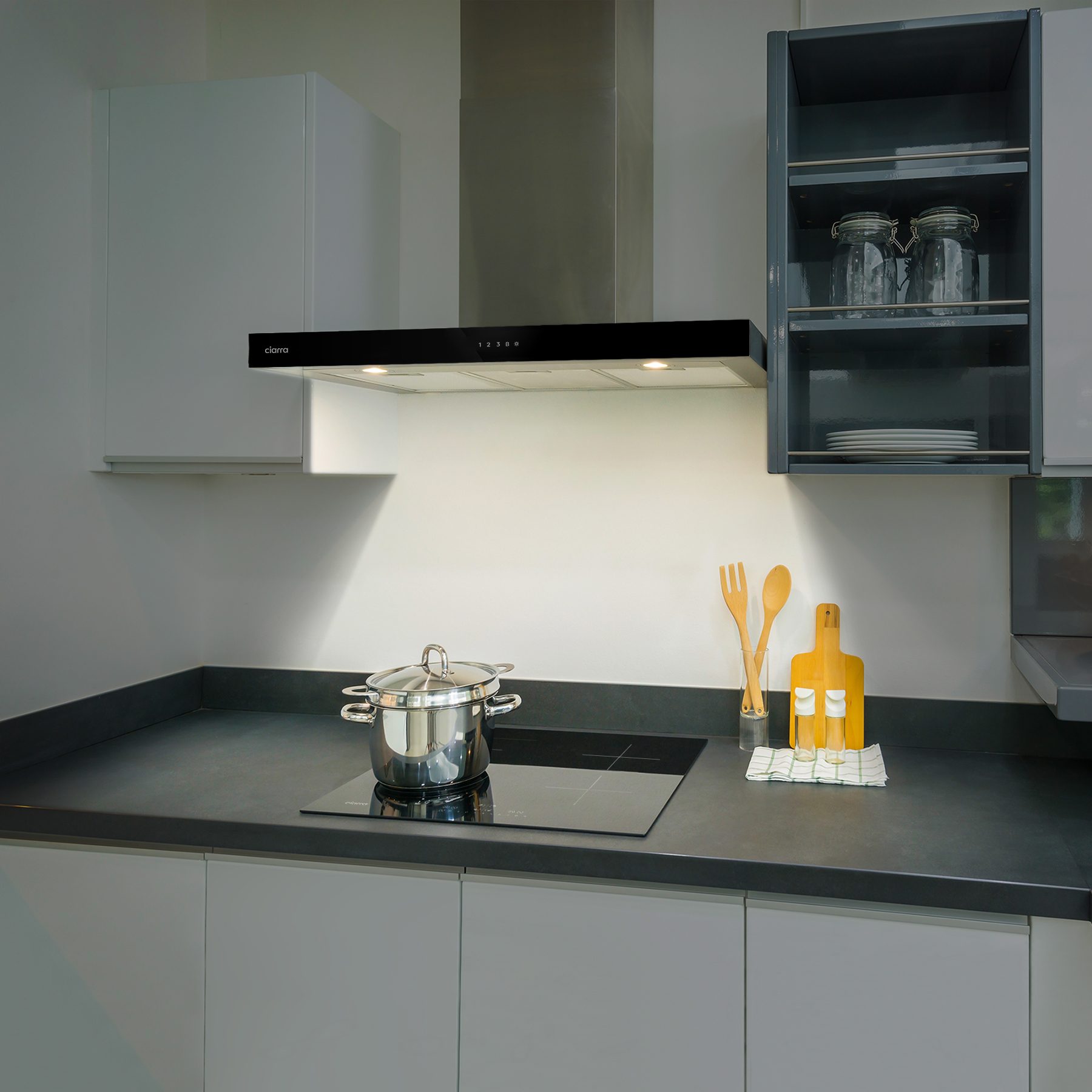 Cucina con cappa nera. Ci sono armadietti, utensili e piano cottura.