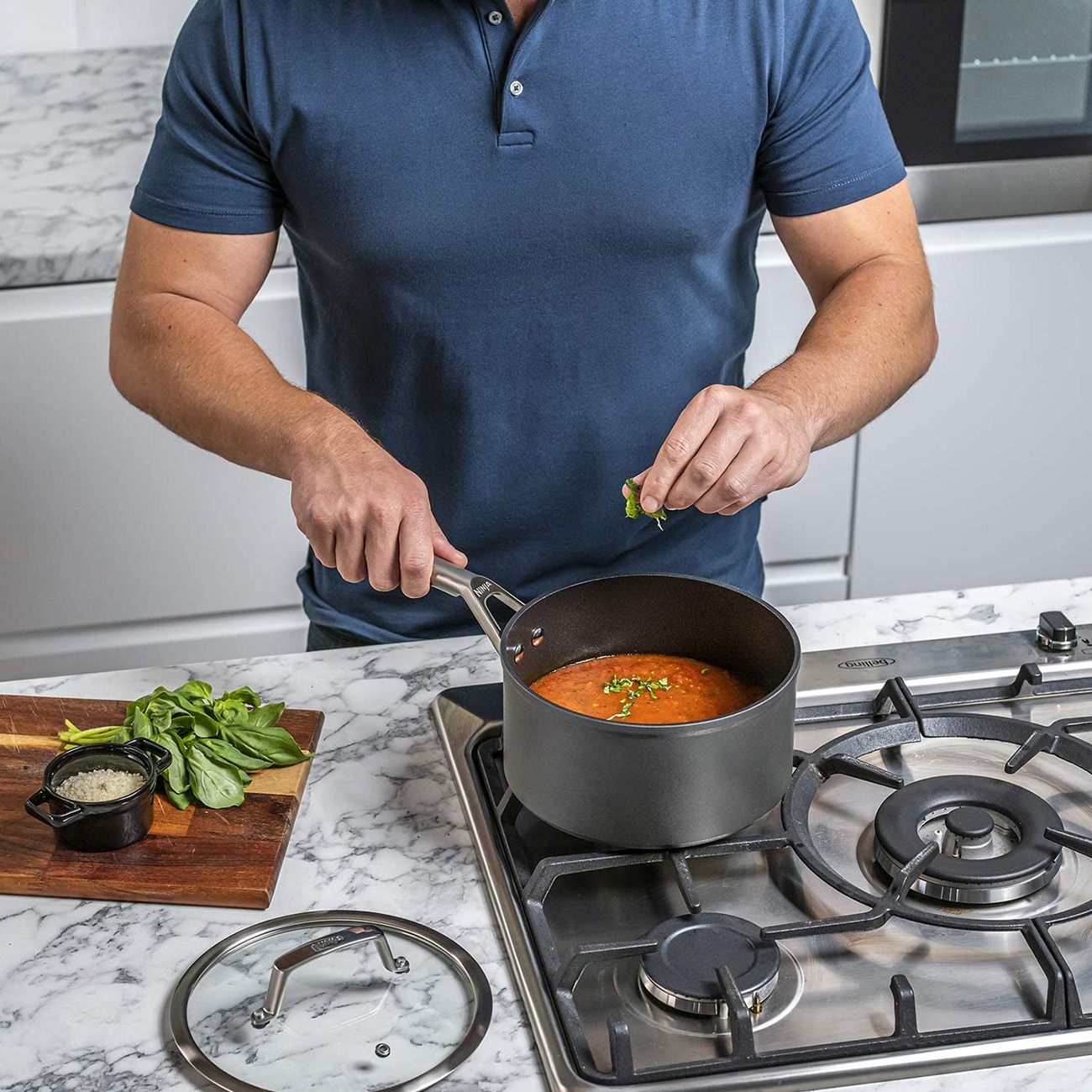 Una persona cucina in cucina. Aggiungono erbe aromatiche a una pentola sul fornello a gas.