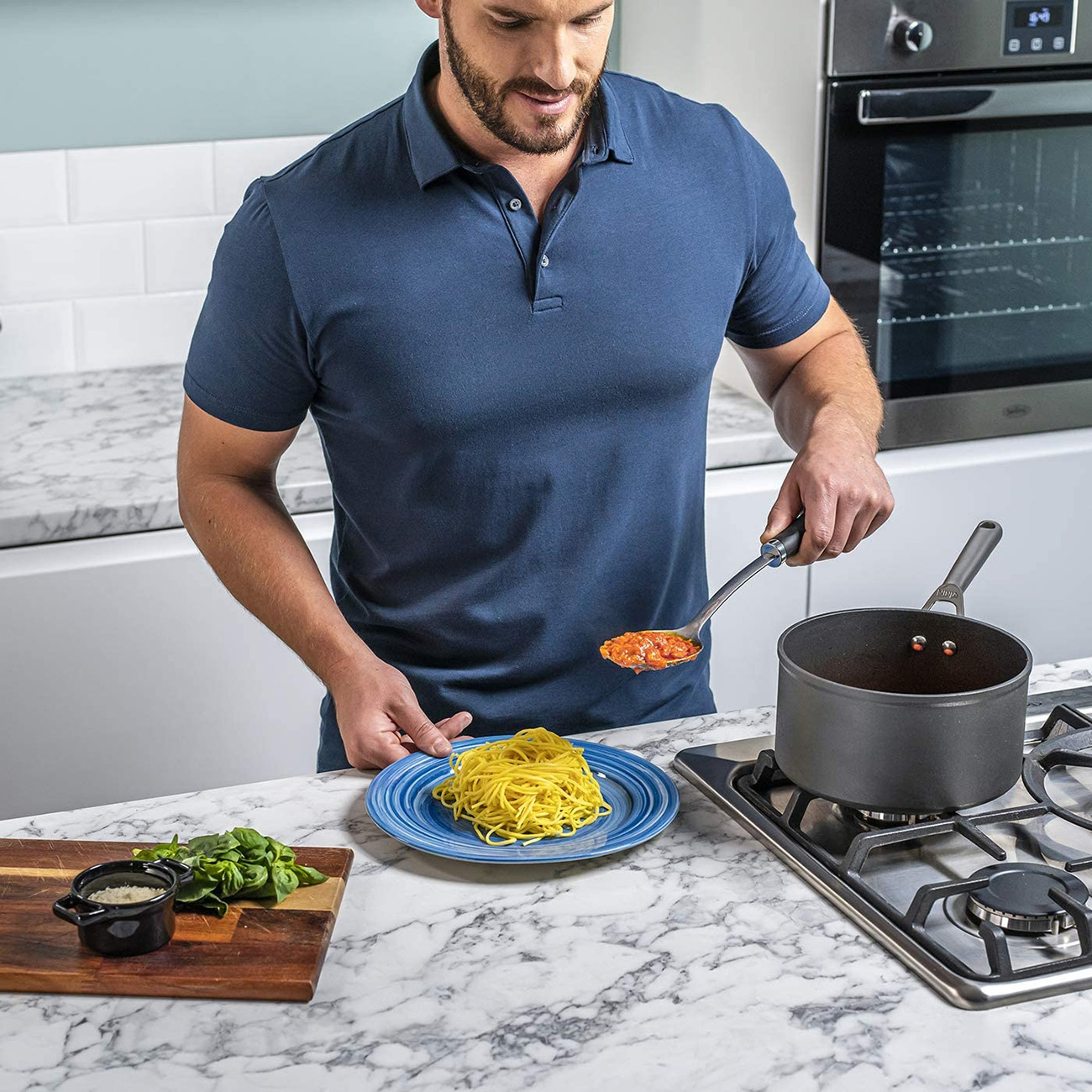 Un uomo prepara la pasta, mettendo la salsa sugli spaghetti. Ambiente cucina con piano in marmo.