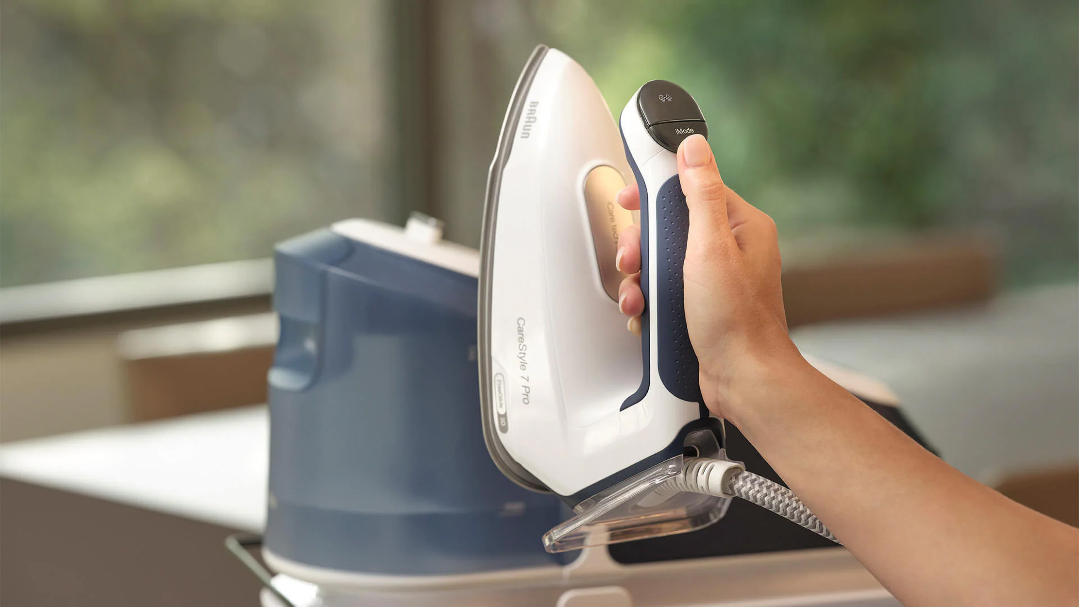 Person's hand holding a white and blue iron, steam coming out.
