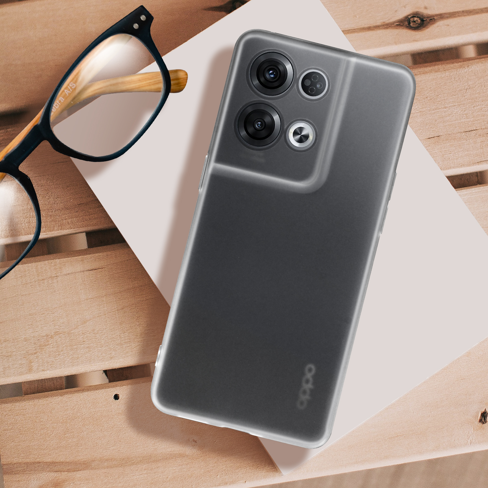 Un telefono grigio con una custodia trasparente, occhiali e una superficie in legno.