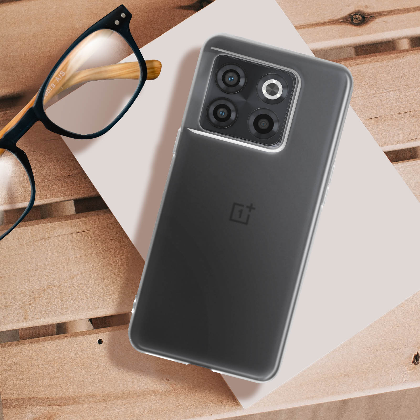 Téléphone dans un étui transparent, lunettes et papier sur surface bois.