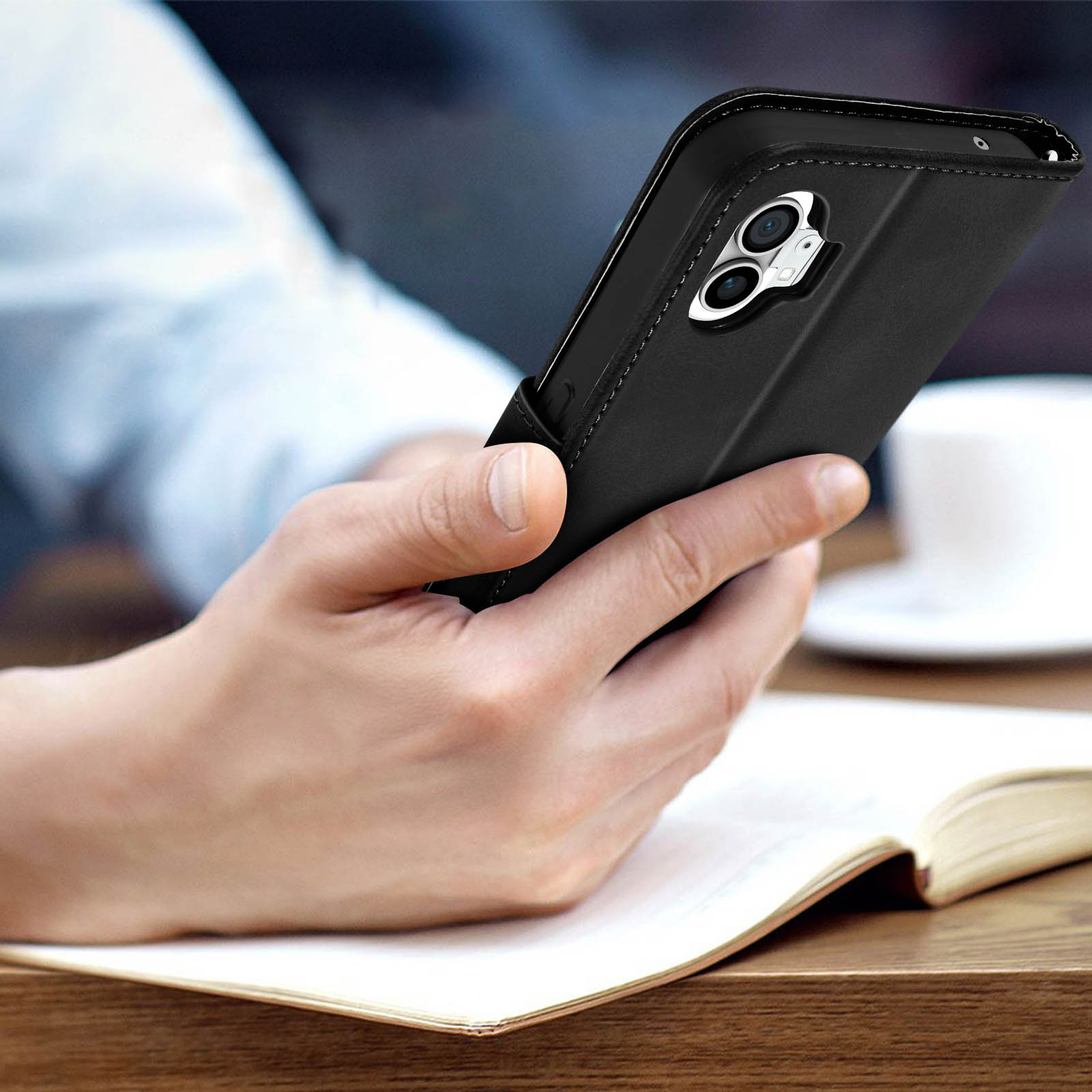Una mano che tiene un telefono nero. Il telefono è in una custodia. Superficie in legno.
