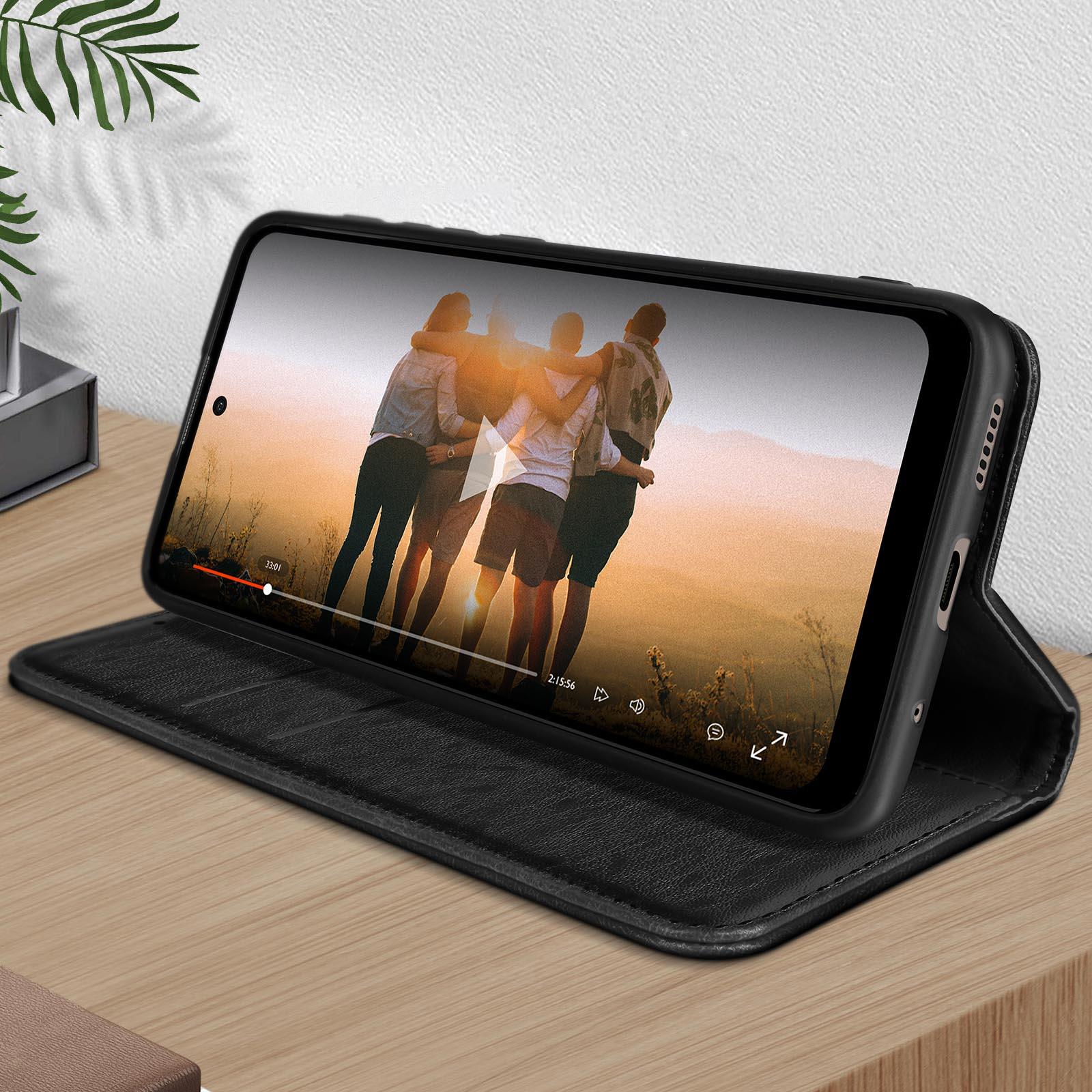 Zwarte telefoon in zwarte hoes op tafel, toont video van knuffelende mensen.
