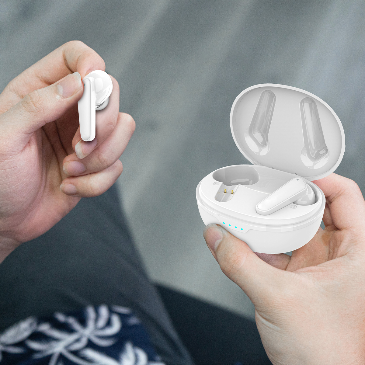 Dłonie trzymające białe bezprzewodowe słuchawki i ich etui ładujące.