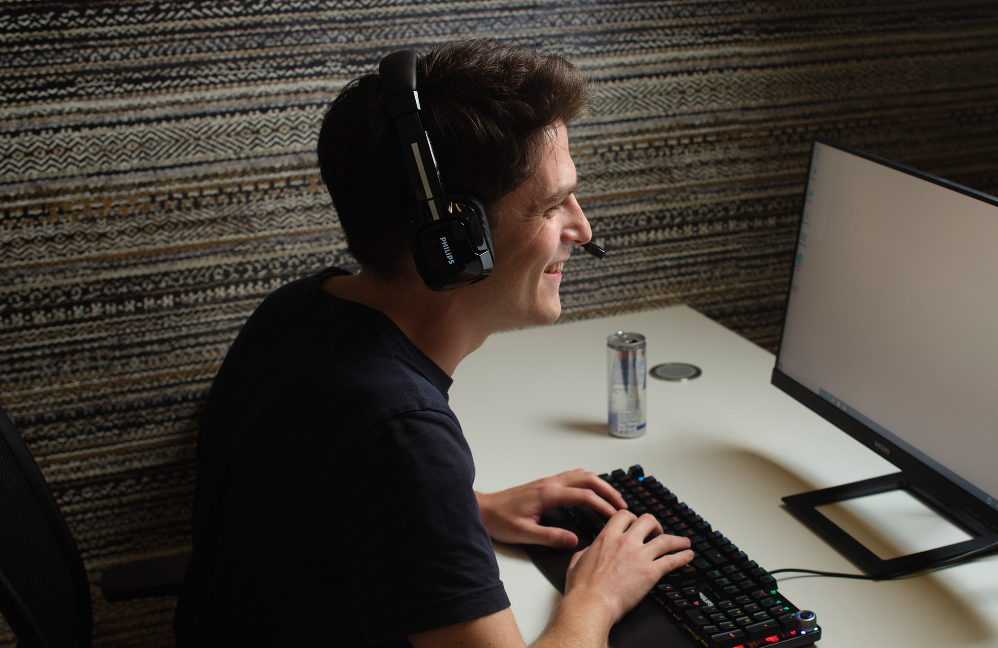 Ein Mann lächelt, trägt ein Headset, schaut auf einen Computerbildschirm und benutzt eine Tastatur.