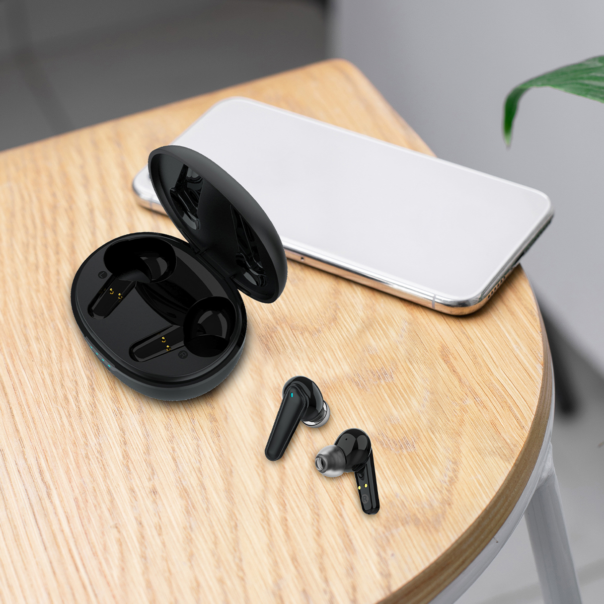 Czarny futerał ładujący słuchawki i dwie słuchawki na drewnianej powierzchni z telefonem.