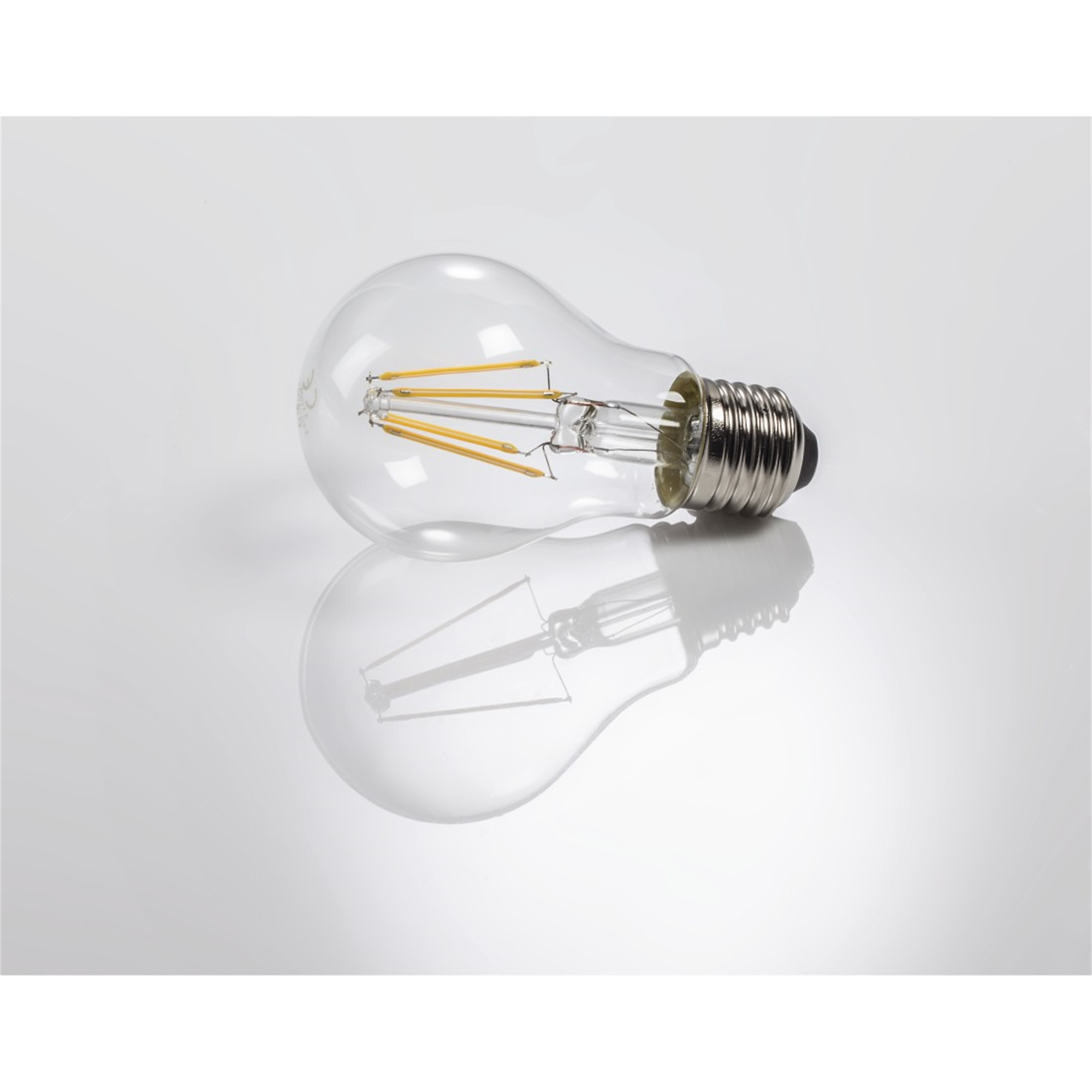 Ampoule transparente avec filaments, sur surface réfléchissante. Fond blanc.