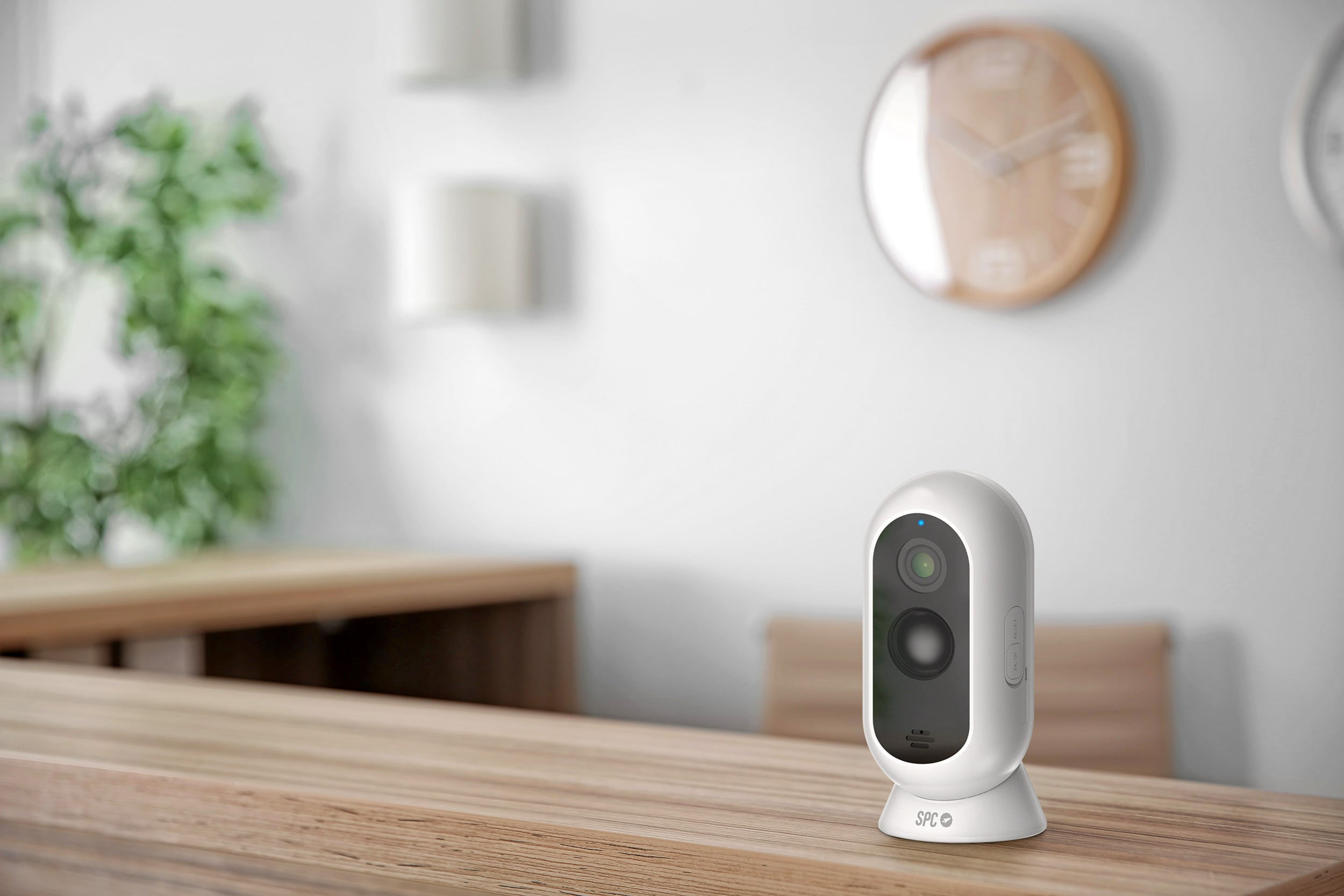 Biała kamera bezpieczeństwa na drewnianym stole, rozmyte tło z białą ścianą.