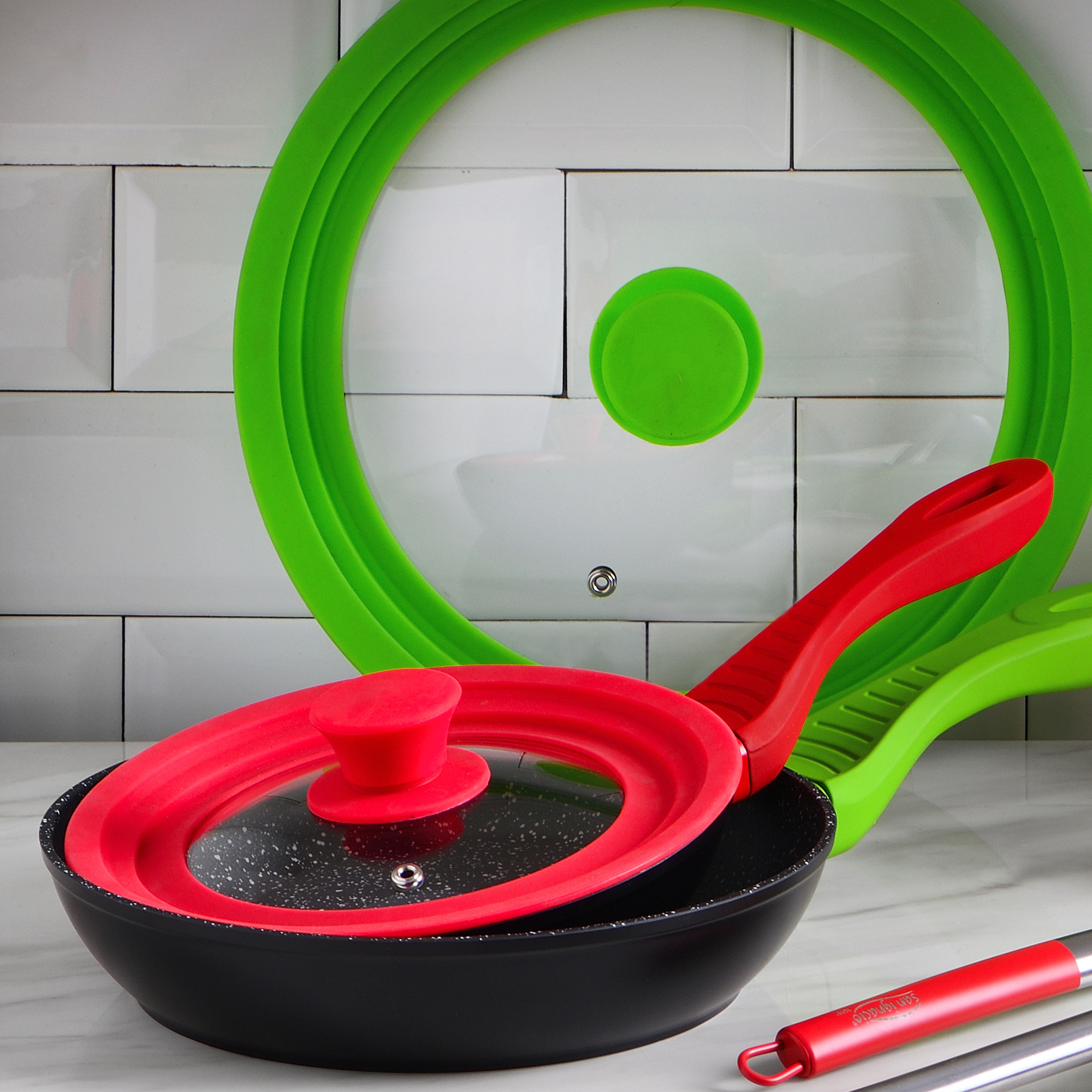 Sartén negra con tapa roja y tapa verde al fondo sobre pared de azulejos.