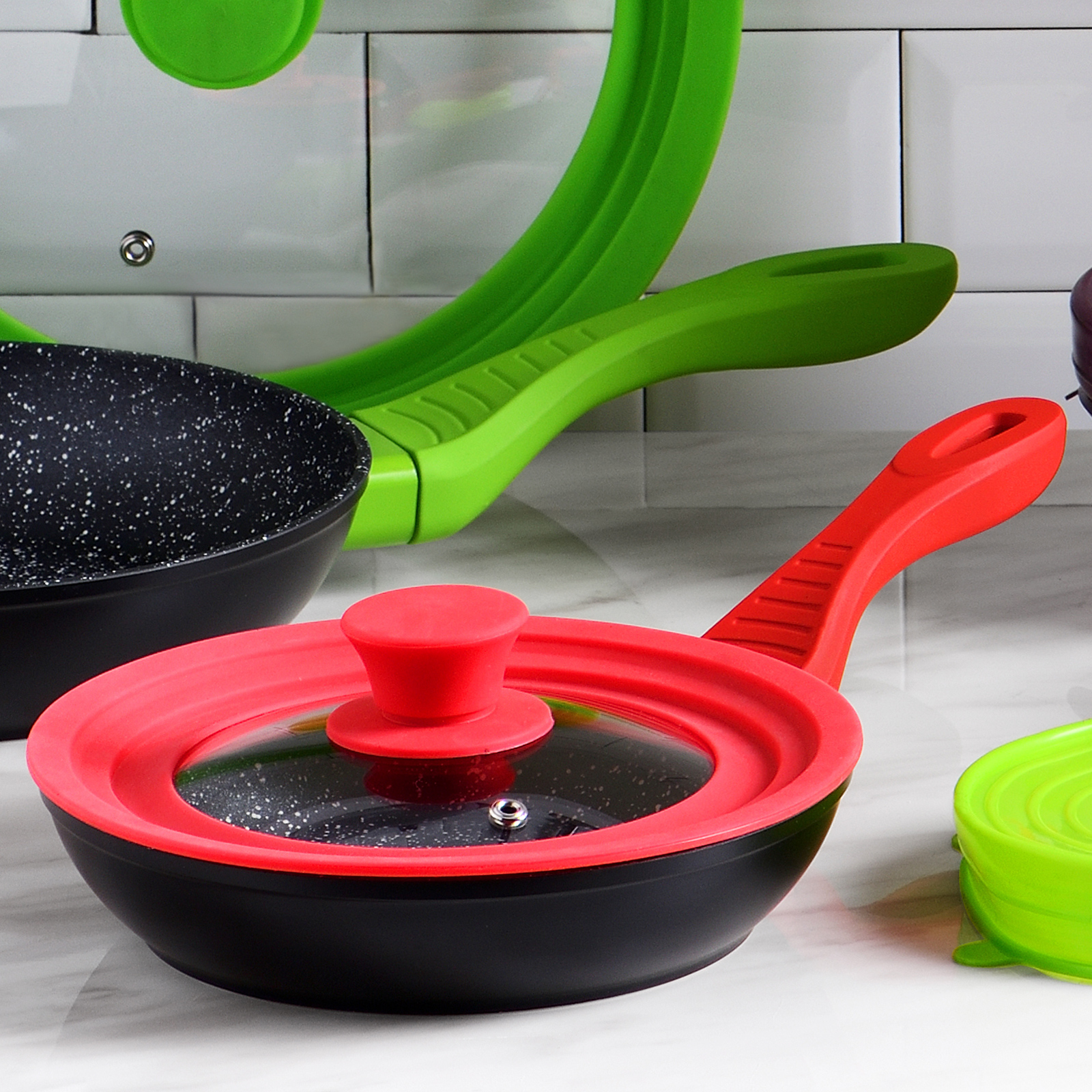 Una olla negra con tapa y asa rojas. Olla verde al fondo.
