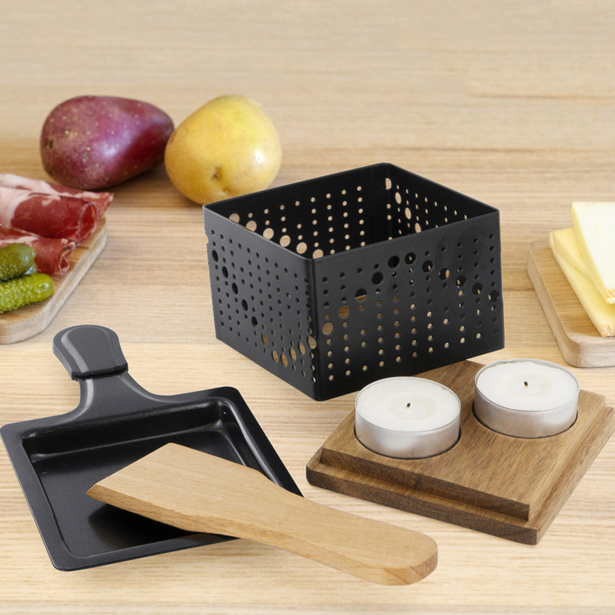 Grill per raclette, cibo e candele su un tavolo di legno, altri oggetti.