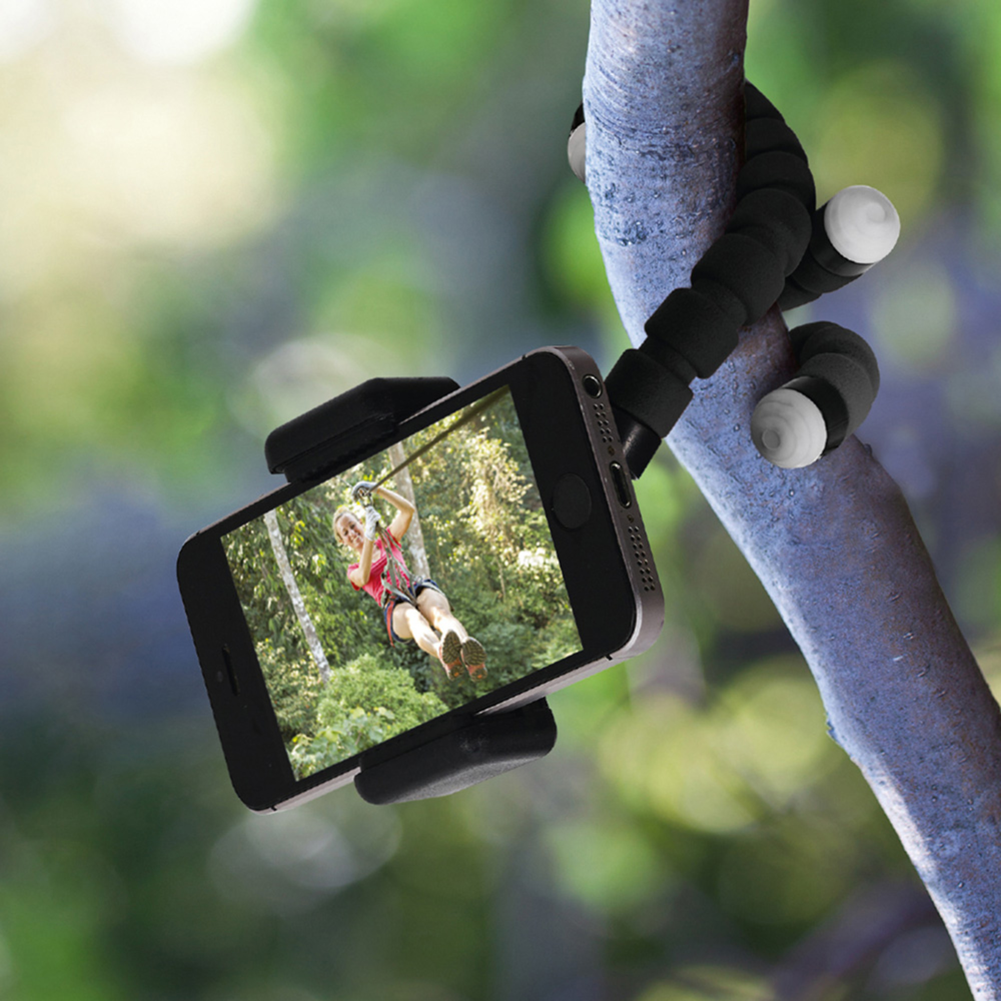 Un teléfono en un trípode flexible. Una persona en la pantalla haciendo tirolesa.