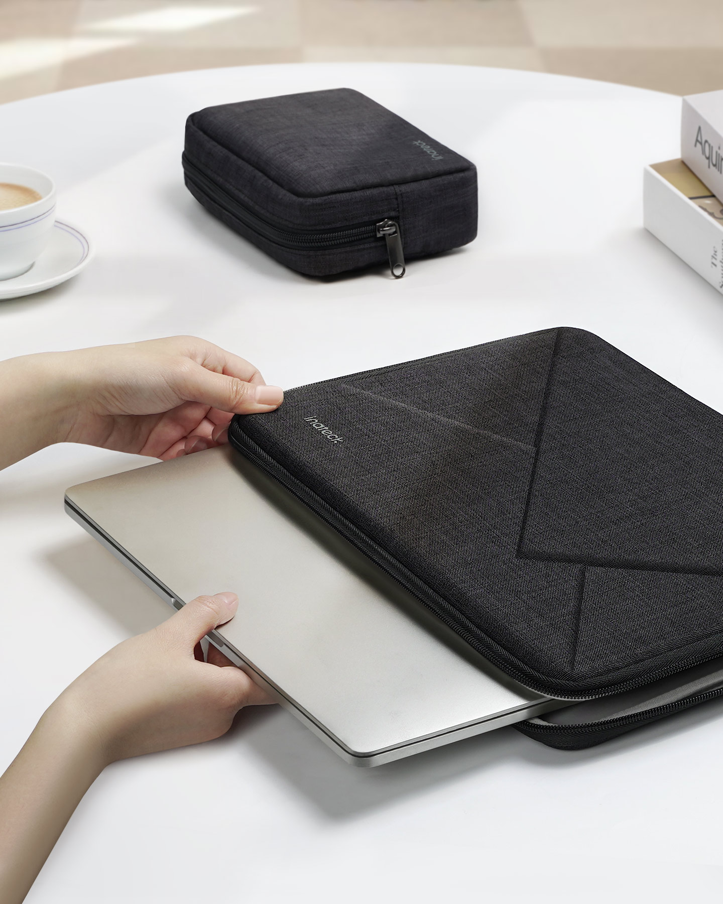Hände halten Laptop und schwarze Hülle auf weißem Tisch.