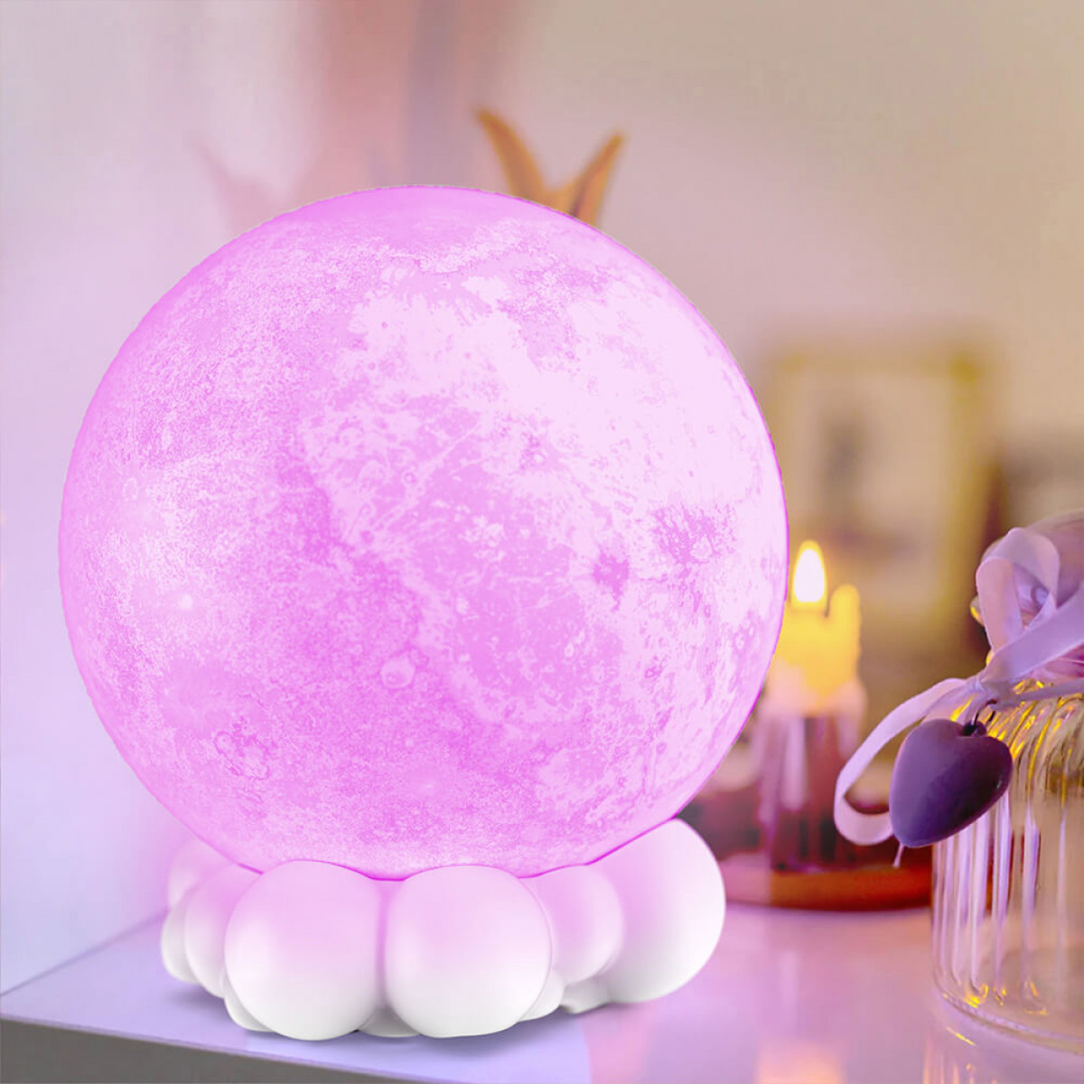 Rosa mondförmige Lampe, die auf einem weißen wolkenförmigen Sockel sitzt. Im Hintergrund befinden sich eine Kerze und ein Rahmen.