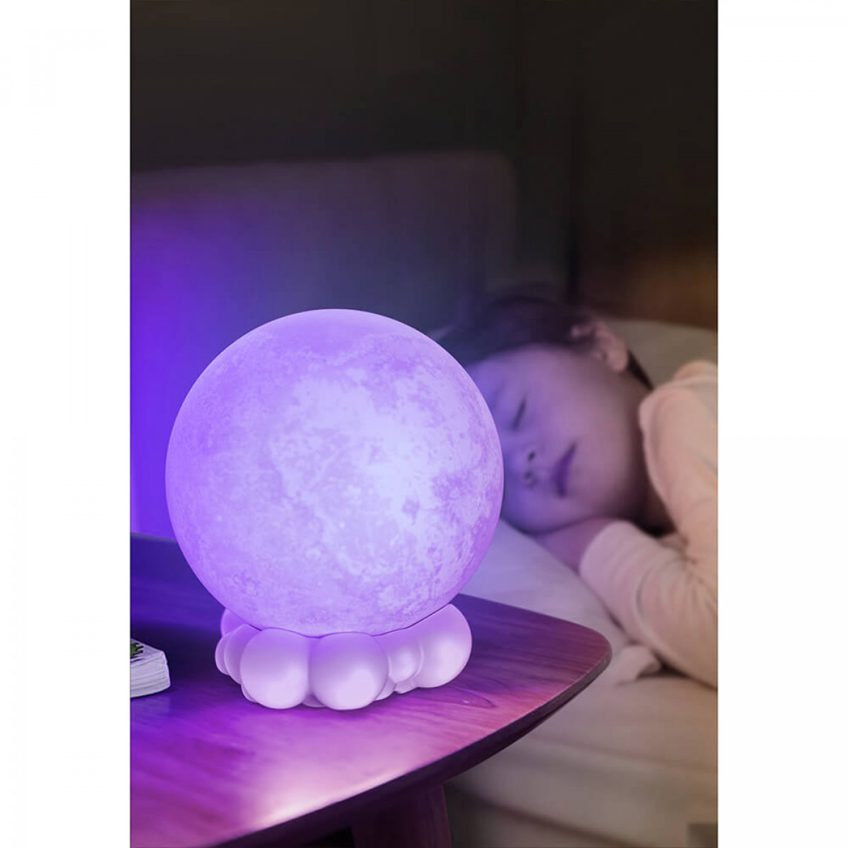 Eine lila Mondlampe auf einem Tisch. Im Hintergrund schläft ein Kind im Bett.