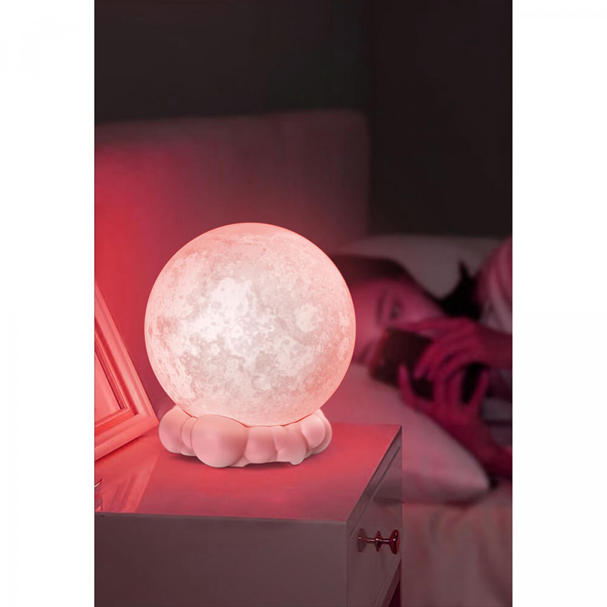 Eine leuchtende Mondlampe auf einem Nachttisch, im Hintergrund eine Person im Bett.