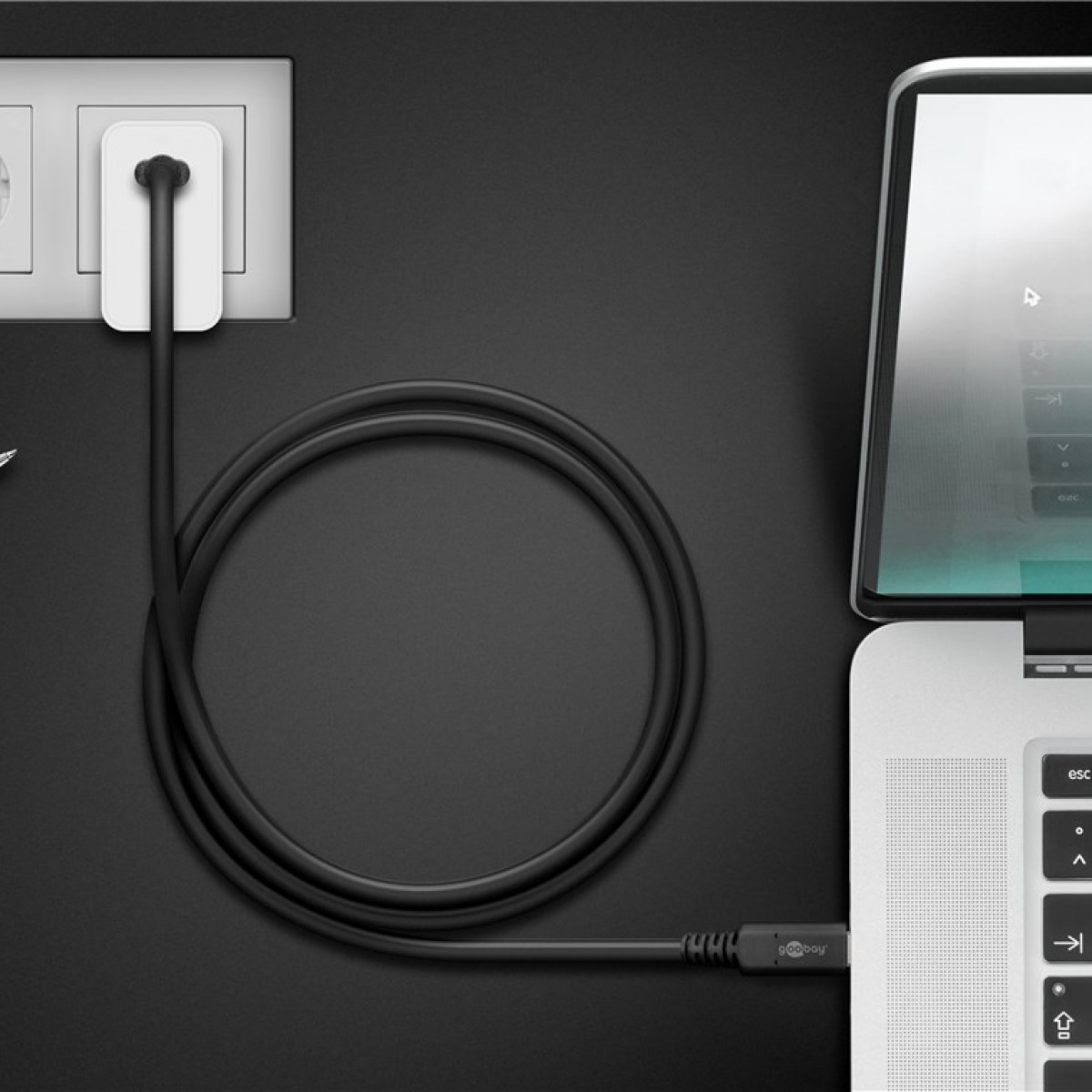 Ein schwarzes Ladekabel, das mit einem Laptop und einer Steckdose verbunden ist. Dunkler Hintergrund.